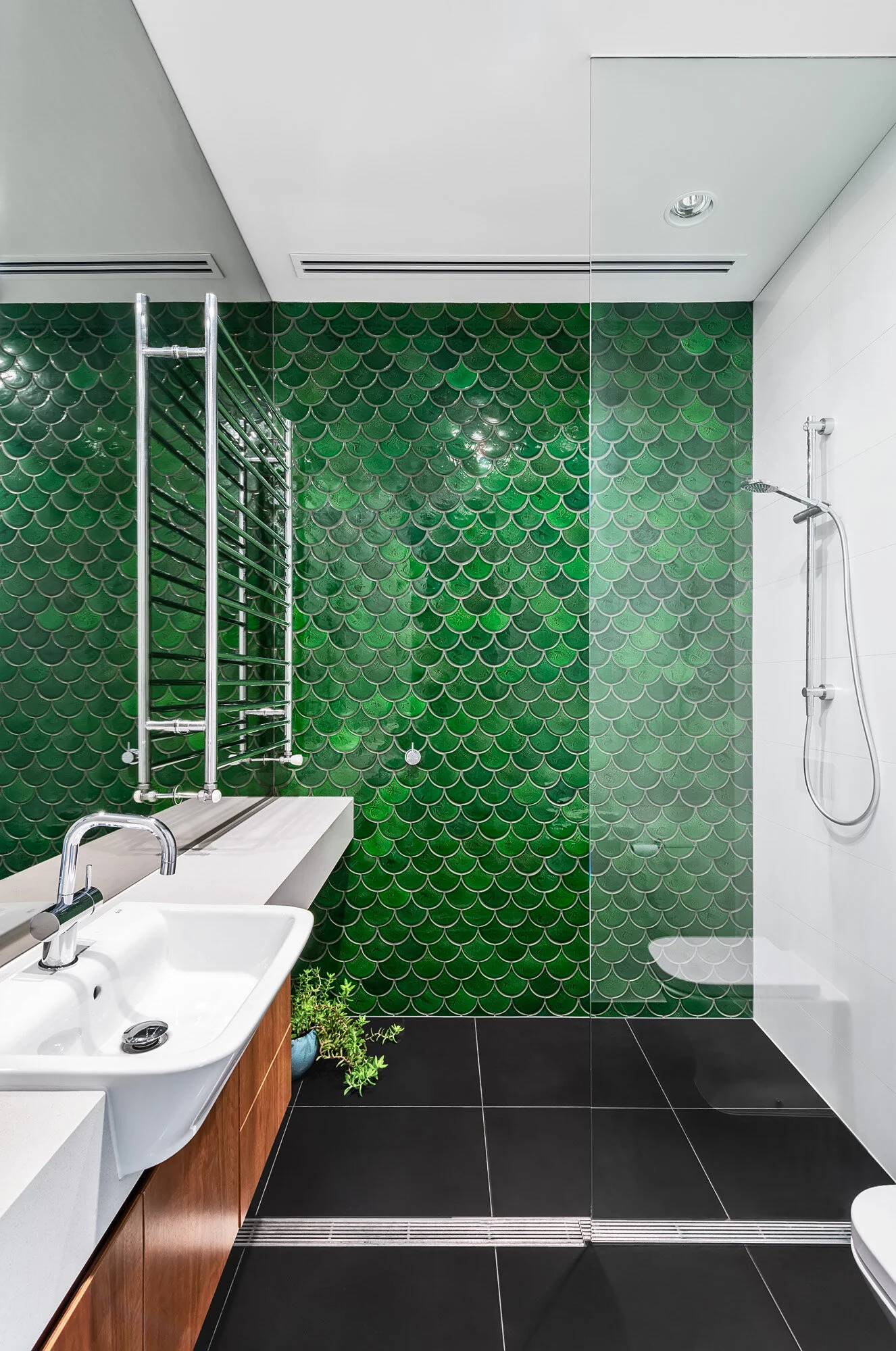 Bathroom with green fish scale tiles and timber cabinetry.