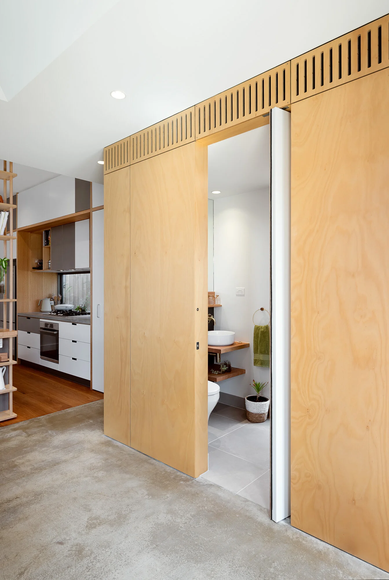 Bathroom with concealed door clad in plywood. Slotted mechanical ducting over