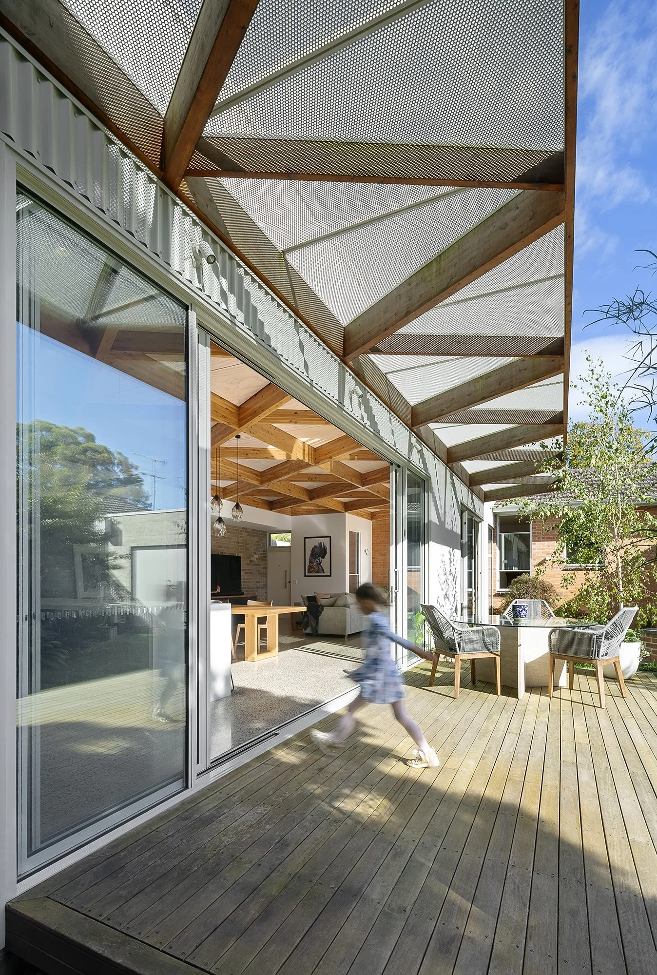 Side view of the perforated steel shading pergola over the deck, with a child running past the outdoor dining table