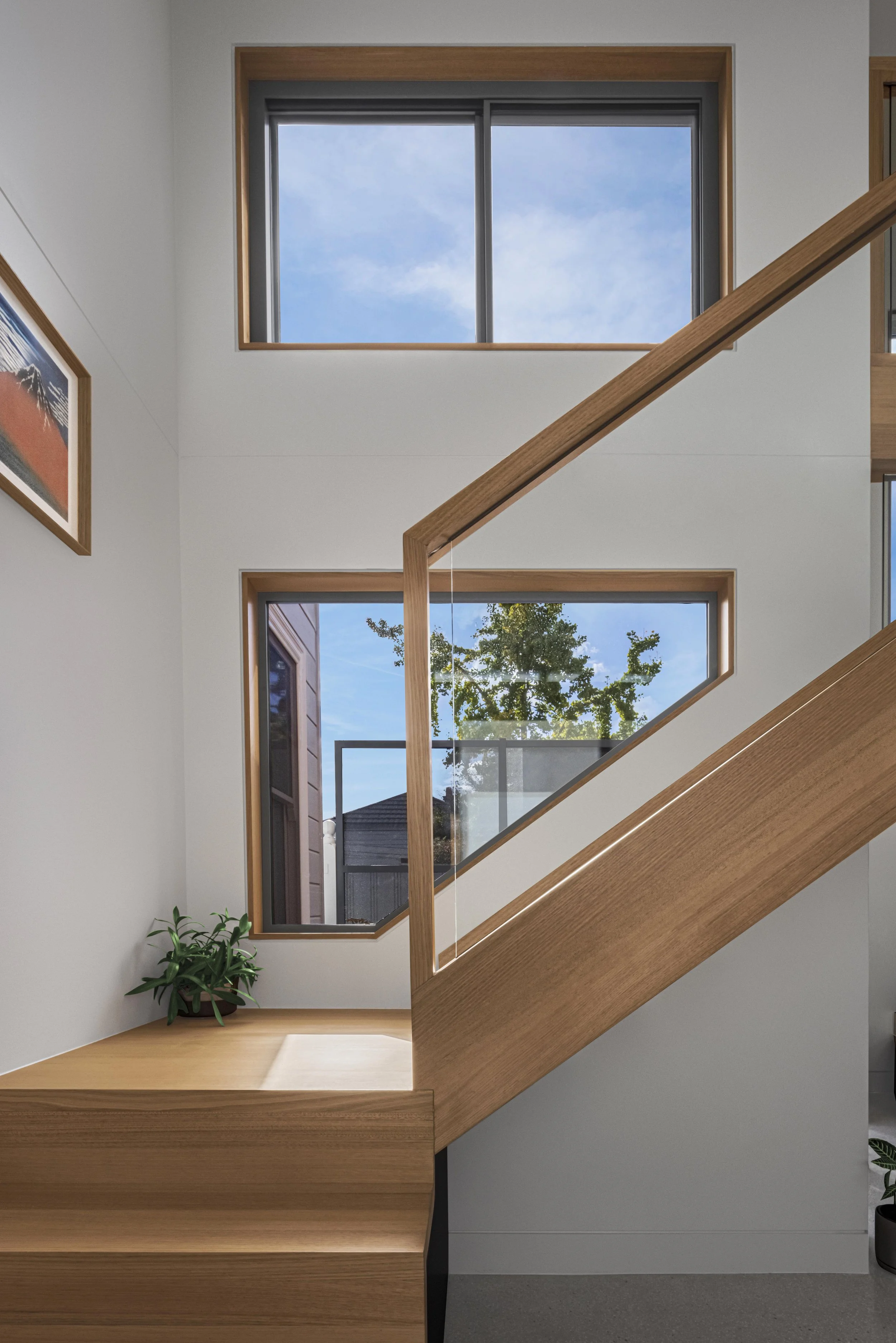 Timber-framed clerestory and garden-facing windows lighting the staircase, with glimpses of the neighbouring rooftop and steel screen
