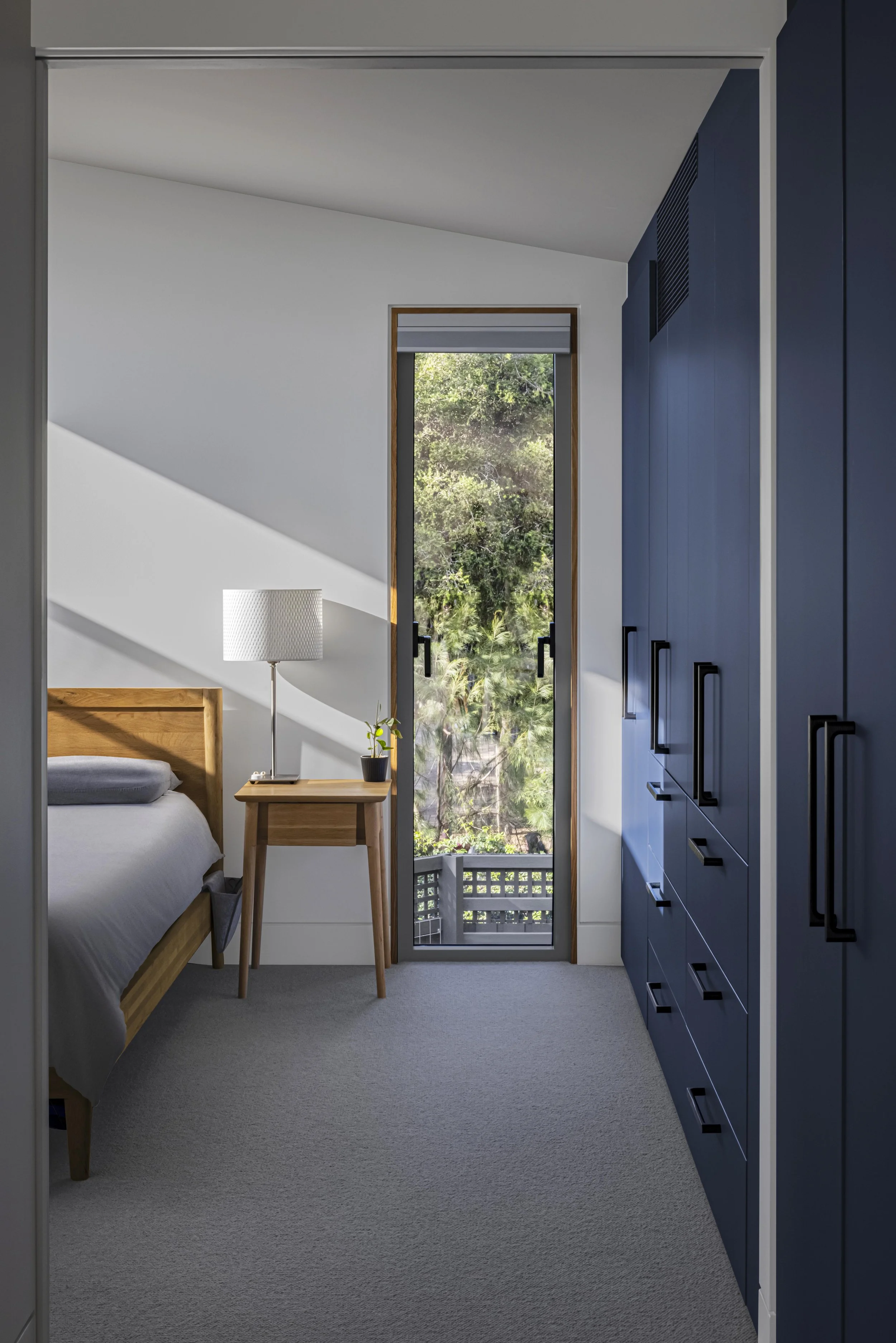 Peaceful bedroom with built-in navy joinery and a tall picture window framing established garden greenery