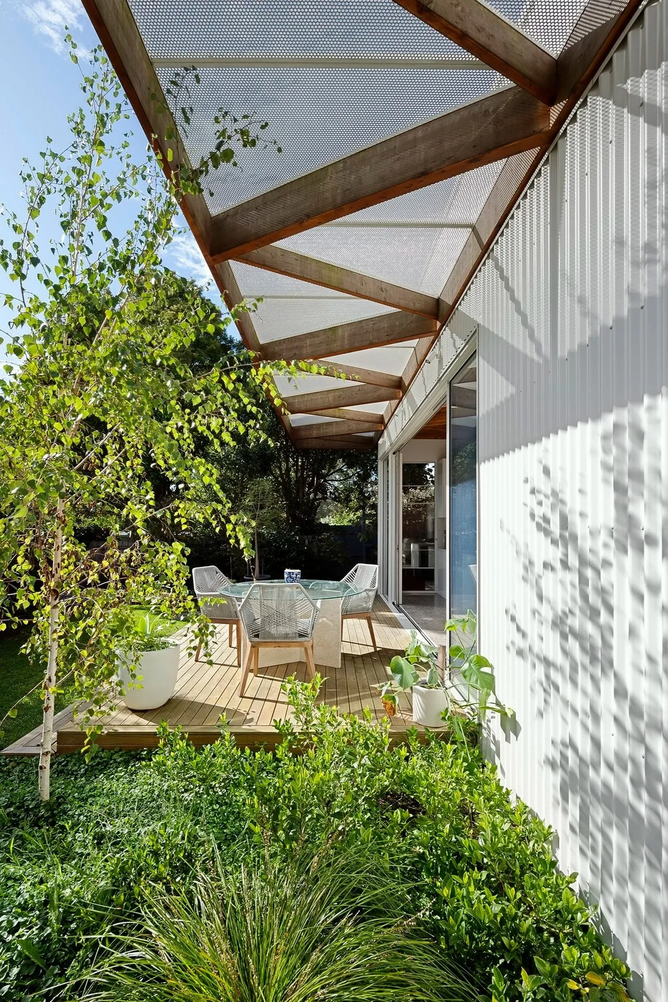 Luscious garden with a perforated metal pergola running over a deck with an outdoor dining table