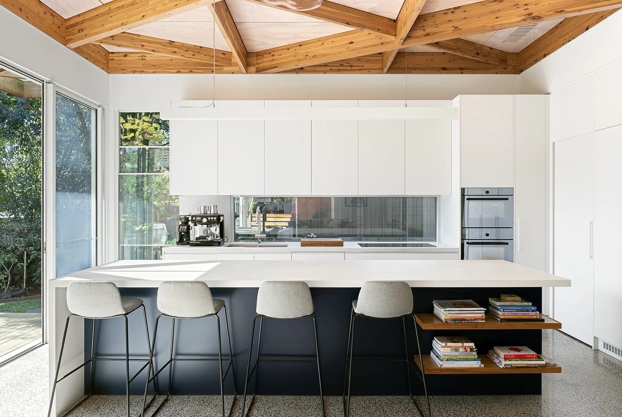 Kitchen island with bar seating and a navy joinery base, with open shelving of cookbooks beneath the benchtop