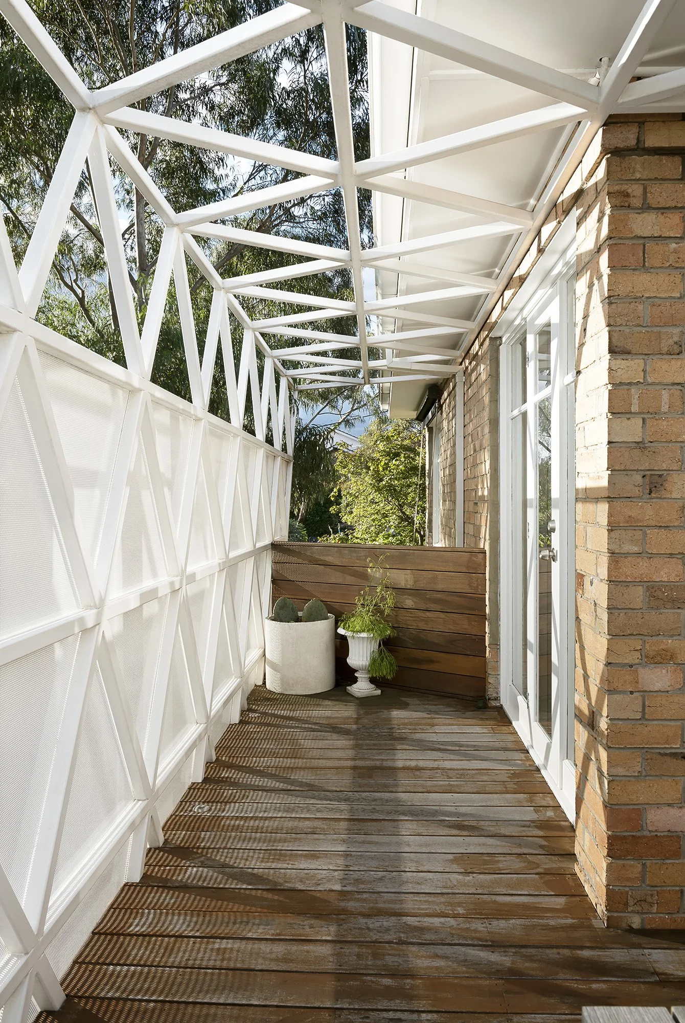 Covered upper-level walkway wrapped in a perforated steel screen, with potted plants beside the brick facade