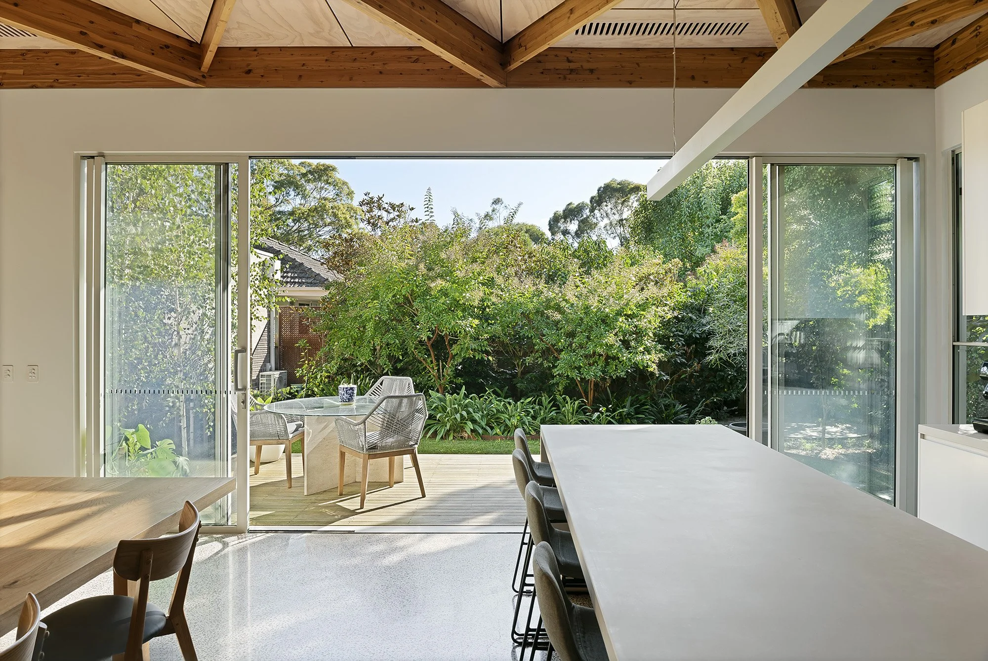 Kitchen and dining space opening through full-height glazing to a timber deck and established garden