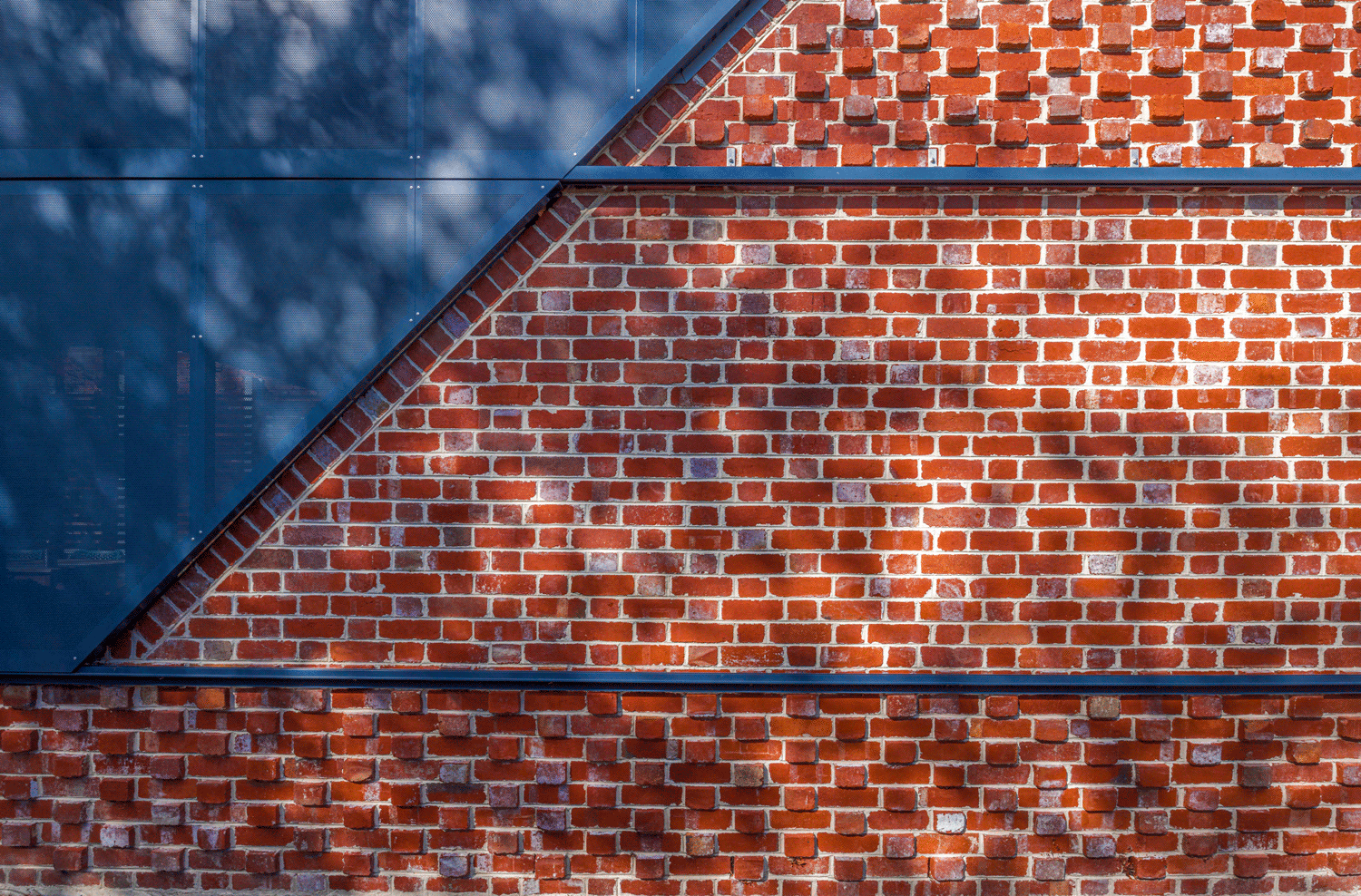 Close detail of layered brickwork and a perforated steel screen panel, showing the junction between materials