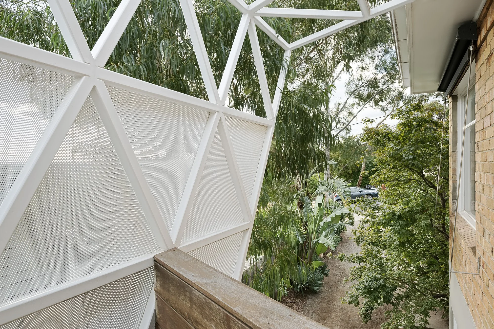 Close-up of the home's triangulated perforated steel sun-shading screen beneath established eucalypt canopy