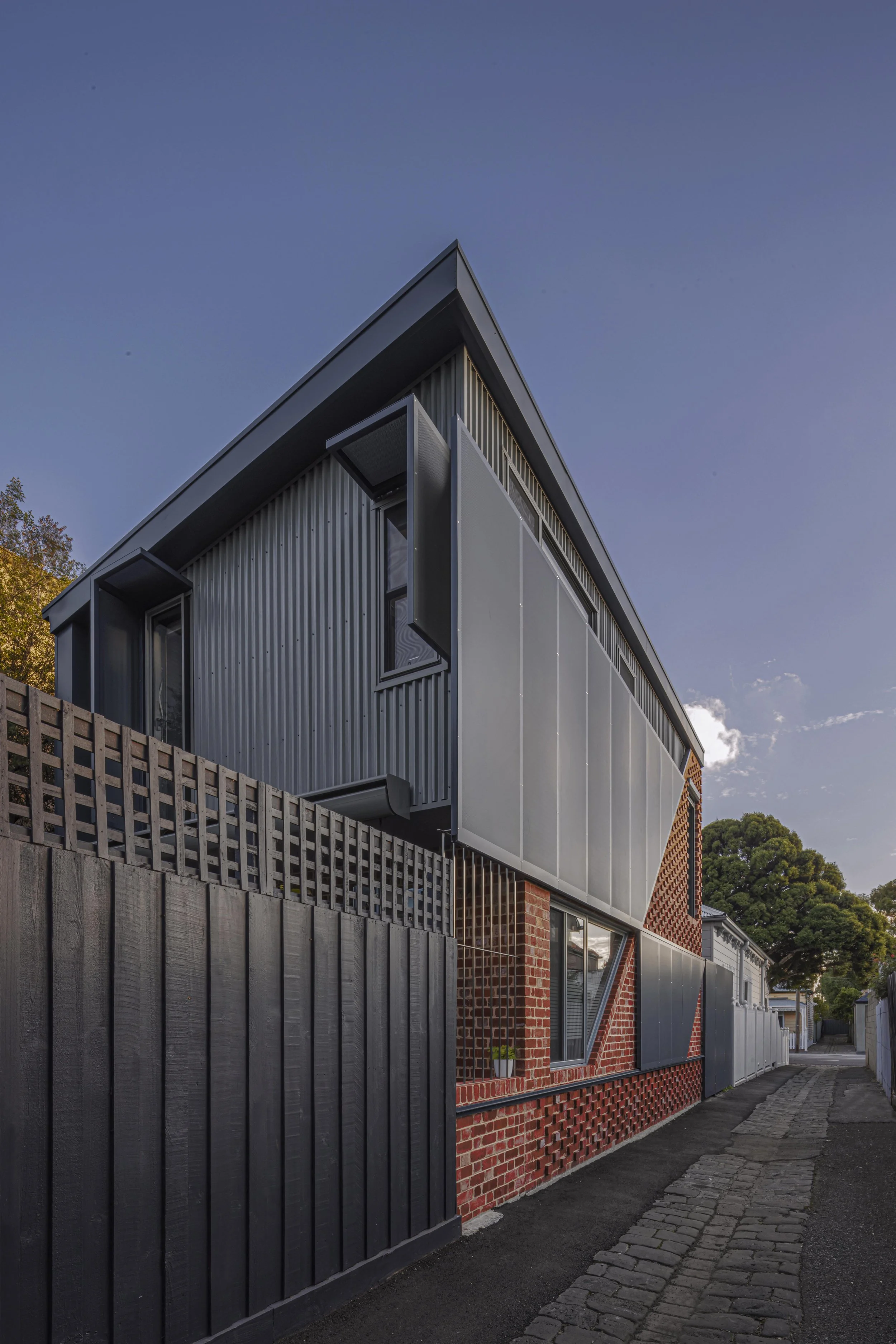 Rear laneway elevation with dark corrugated metal cladding, a perforated steel privacy screen and recycled brickwork below