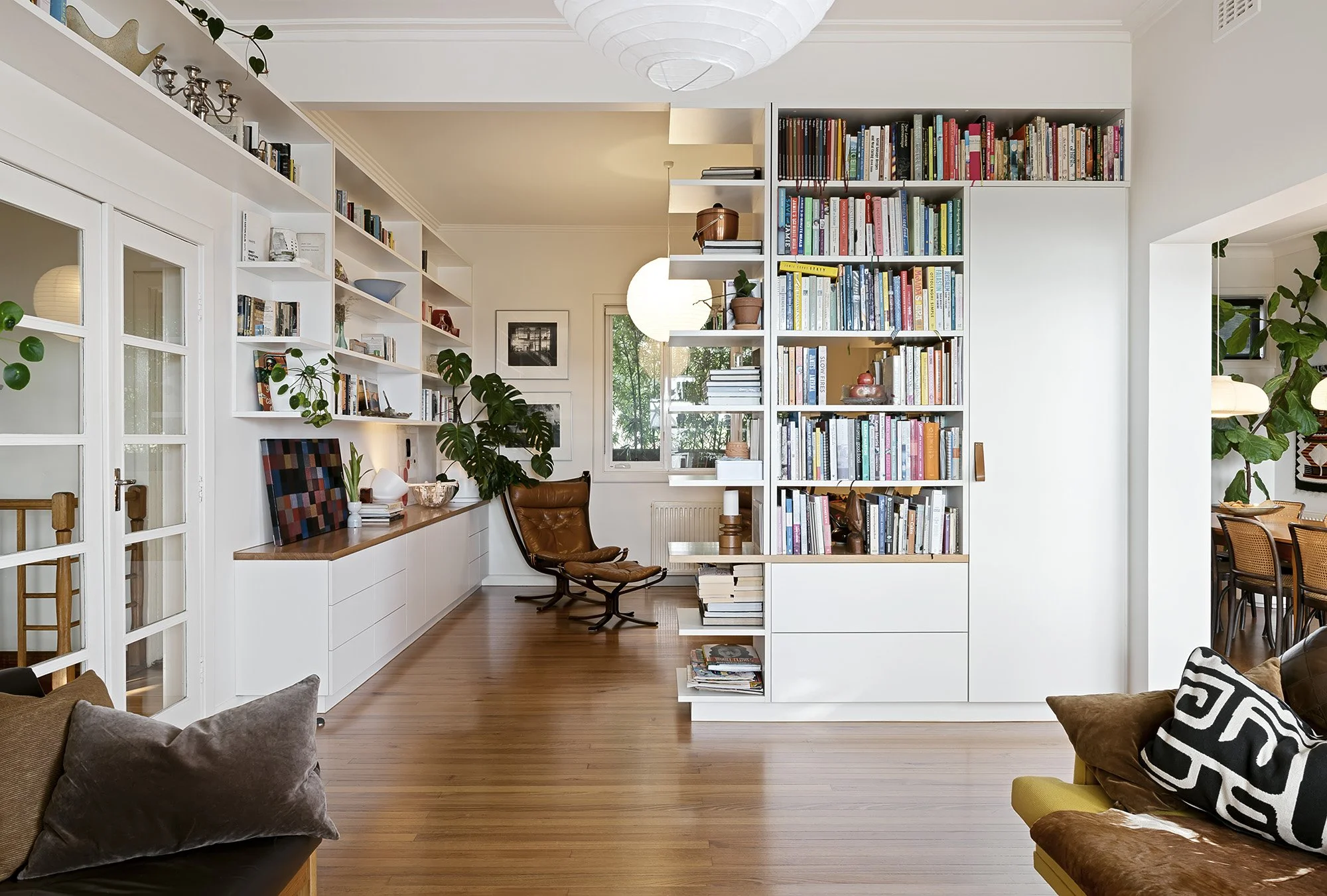 Long open-plan living and study space with a floor-to-ceiling bookcase, paper pendant lights and timber flooring