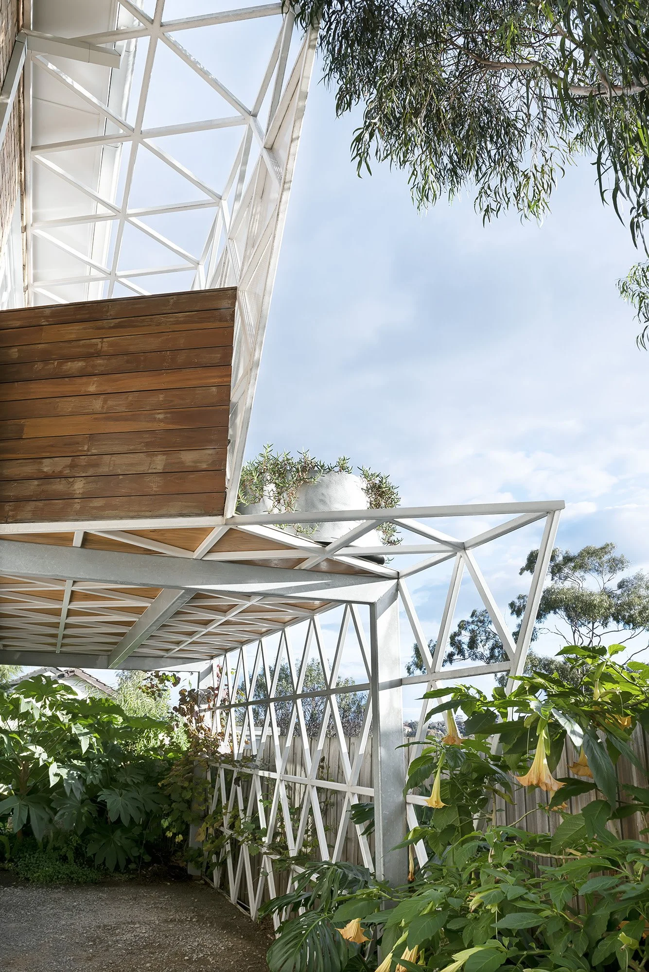 Rear carport extension with dark timber cladding and a perforated steel screen rising above a lush native and subtropical garden