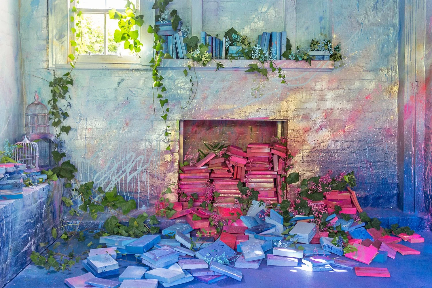 Red and blue books spill out of a painted fireplace, greenery sprouts up between books.