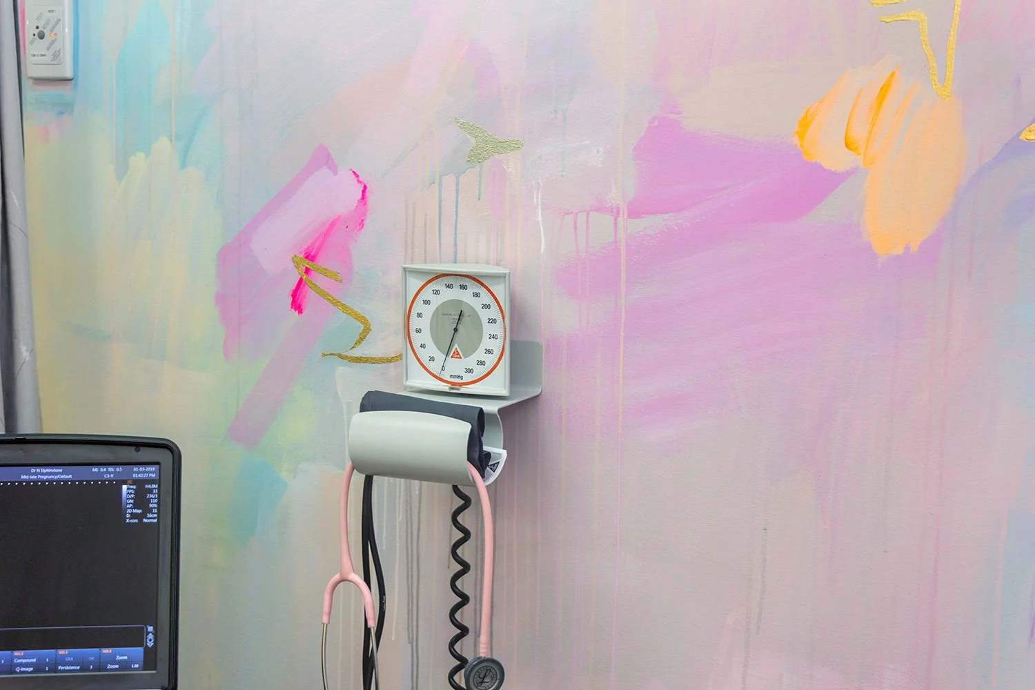 Close up of pastel abstract mural painted in an OB/GYN office, featuring pink stethoscope, medical equipment and neon paint details.