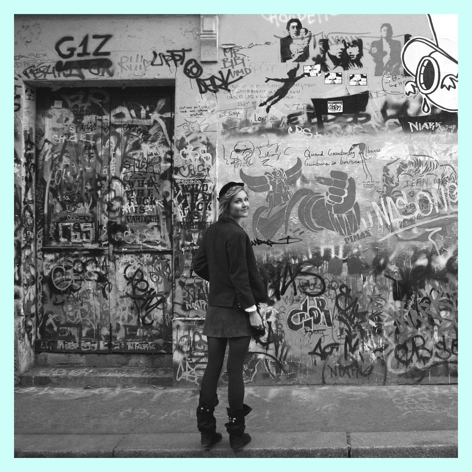 Camille Javal Hayton stands in front of graffiti wall in Paris, her hair in braids she wears knee high black velvet boots, a vintage suede skirt, navy sailor jacket and black French hat.