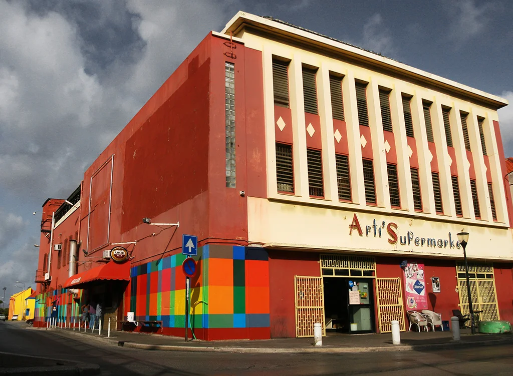 Haas & Hahn community mural project in Curacao, workshop part of Favela Painting Academy, design features brightly colored geometric squares that wrap around the building like woven fabric.