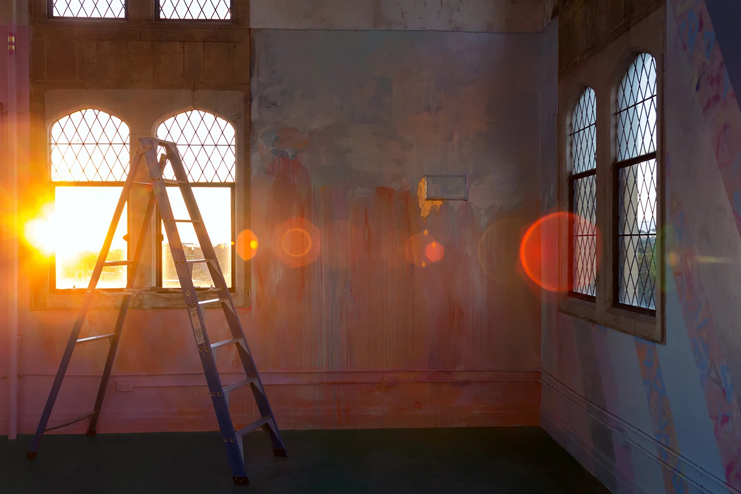 Lens flare creates light rainbow patterns as setting sun streams warmly through window, bounces light on the abstract mural.