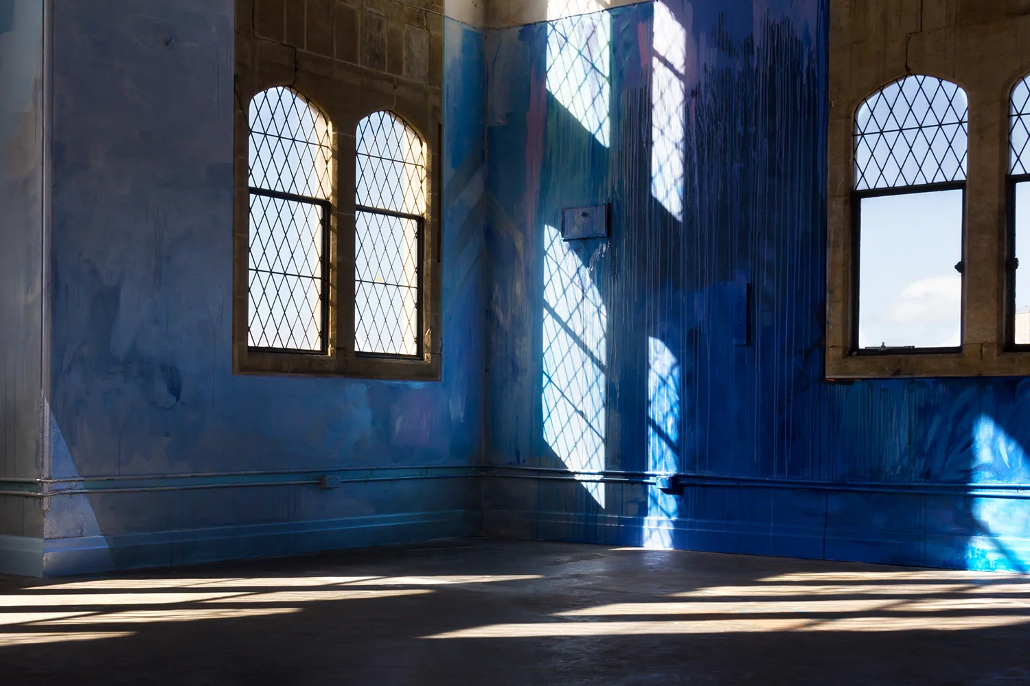 Large scale abstract mural in shades of dark blue and metallic paint, reflected patterns of light project onto the floor and walls.