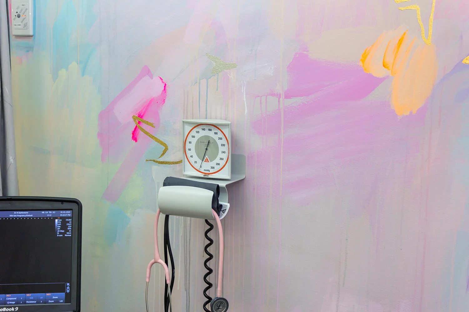 Close up of pastel abstract mural painted in an OB/GYN office, featuring pink stethoscope, medical equipment and neon paint details.