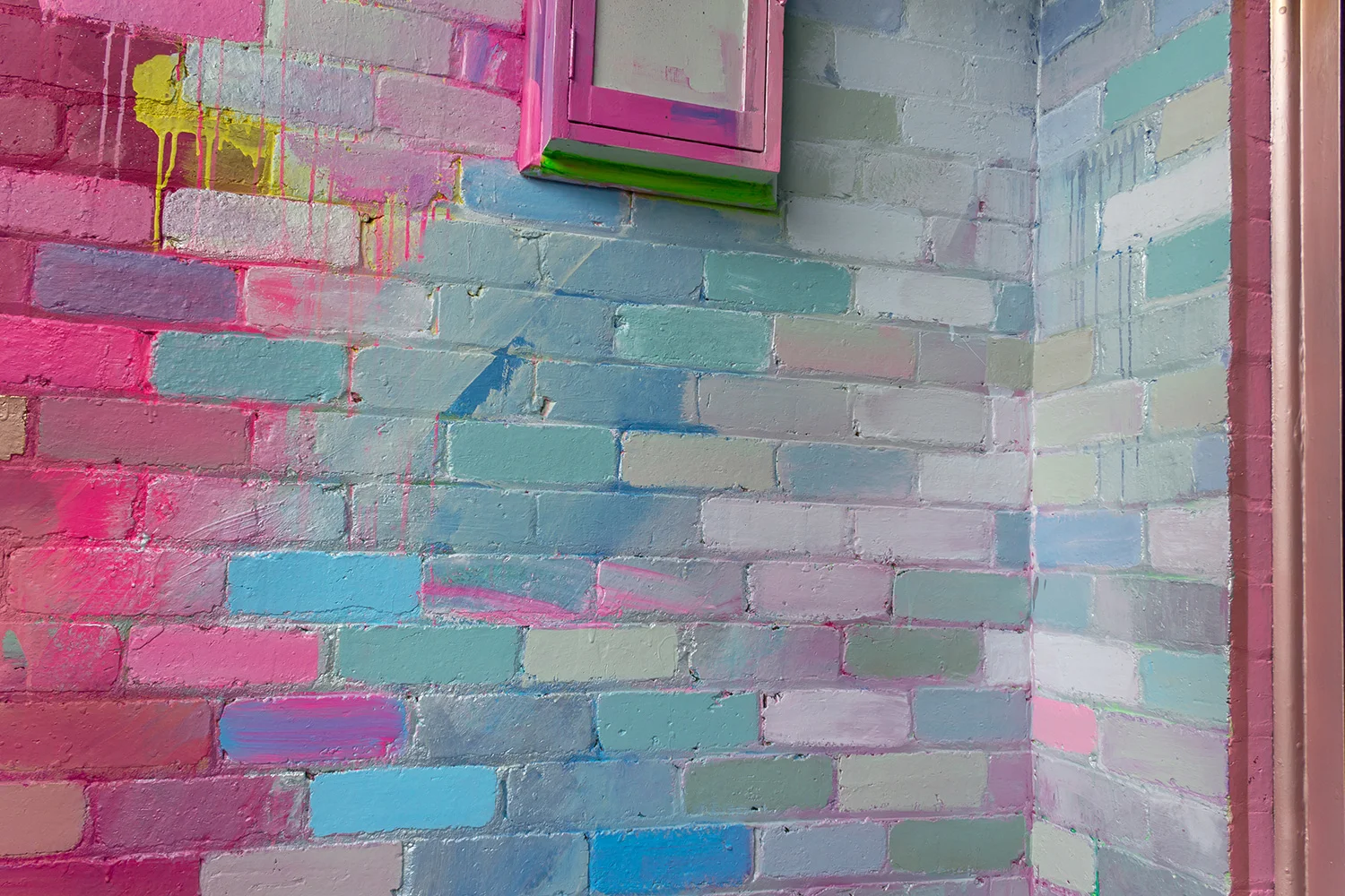 Close up wall detail of abstract mural, showing pink and blue bricks.