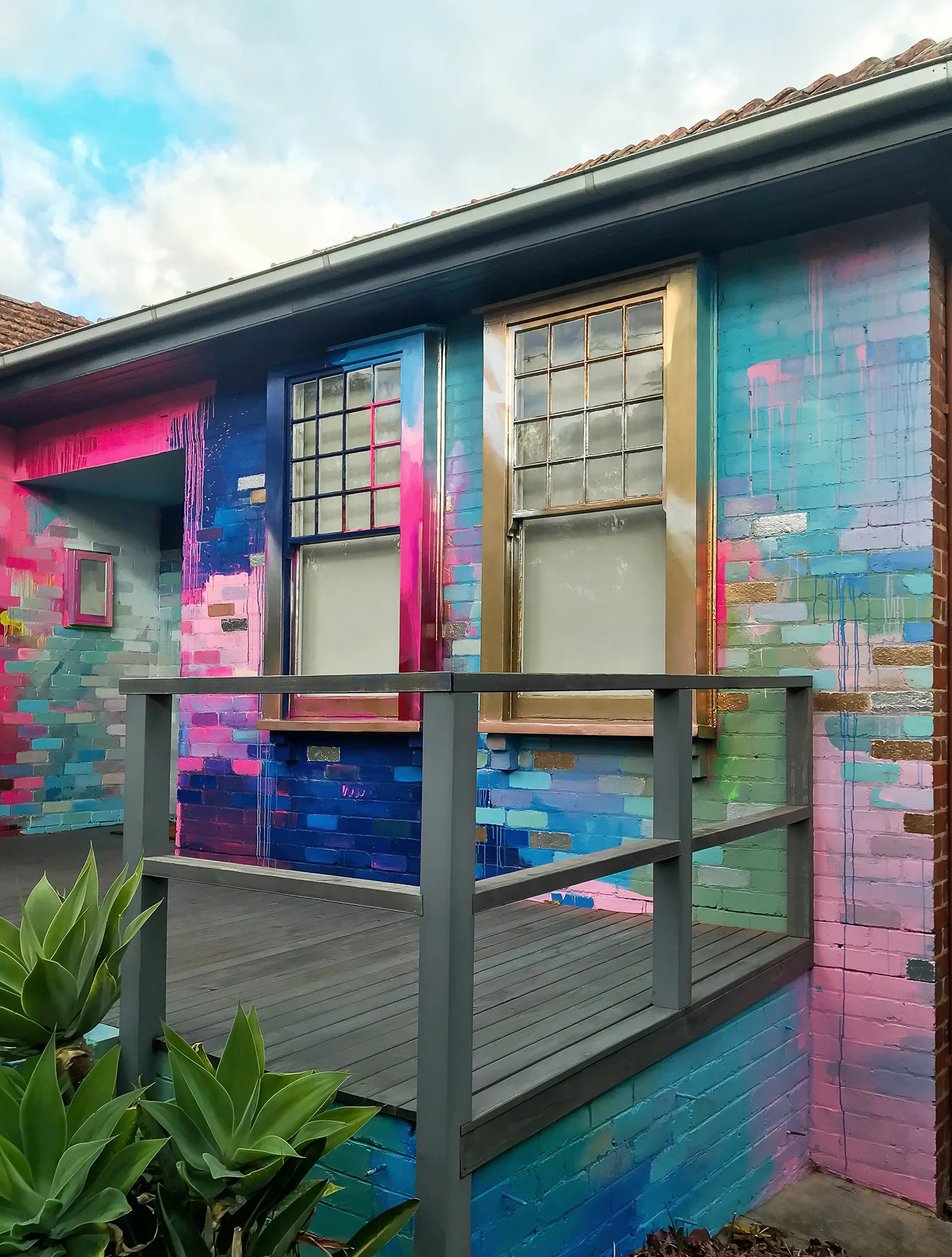Vibrant abstract mural painted on the exterior of a house. The colors contrast with the traditional architecture of the house and surrounding natural elements.