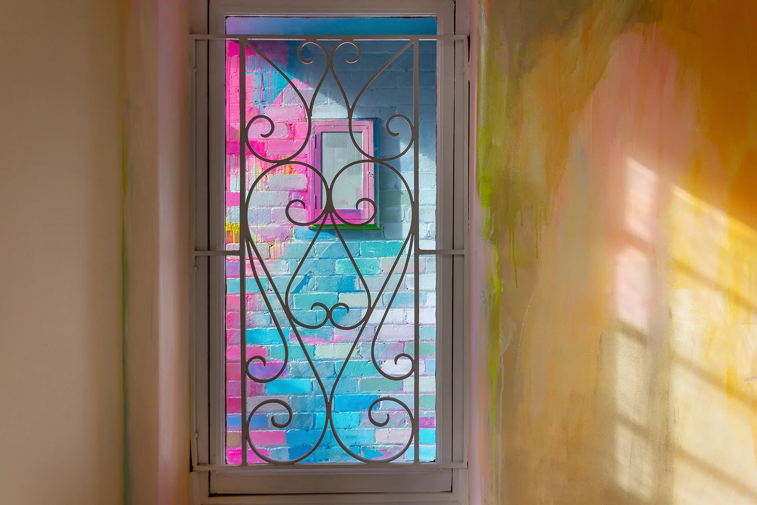 A window provides a glimpse at a vibrant abstract mural on the wall outside.
