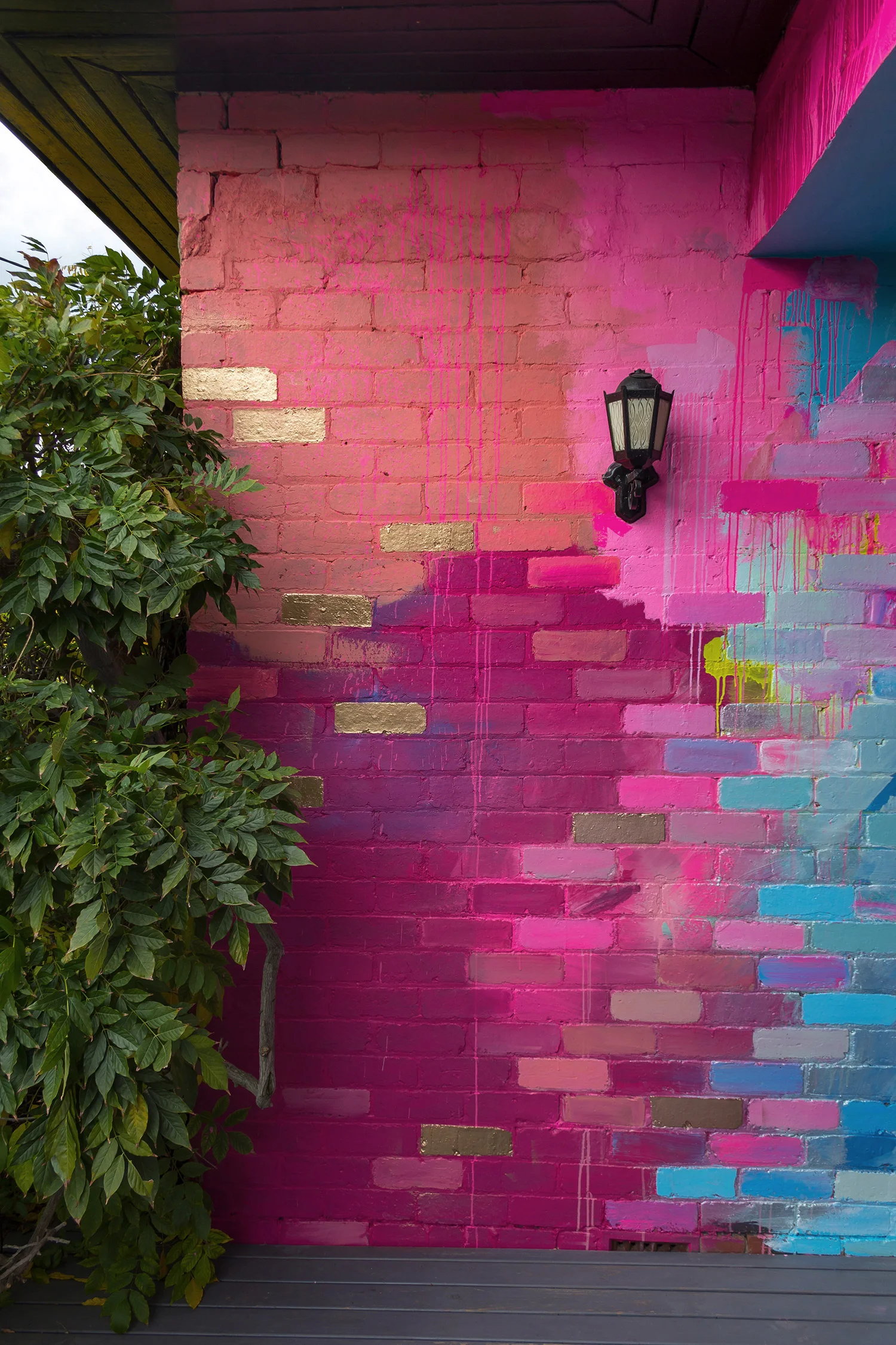A residential home has been used as a giant art canvas, with a vibrant, abstract design painted on the bricks in a color palette of pink, blue and metallic.