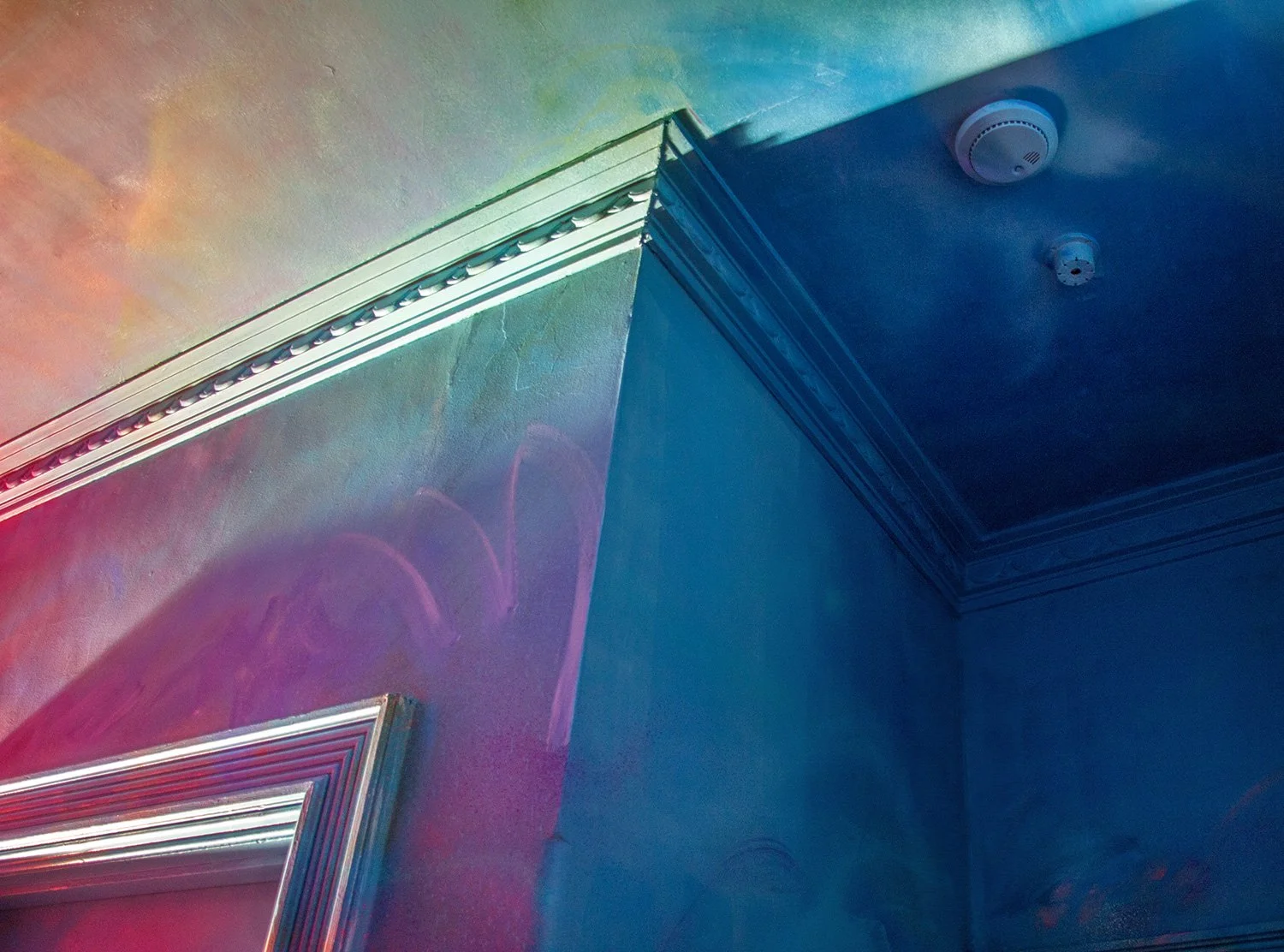 Close up of mural corner detail showing rainbow colors - blue, purple, green, yellow and red - the paint moves from the walls up onto the ceiling.