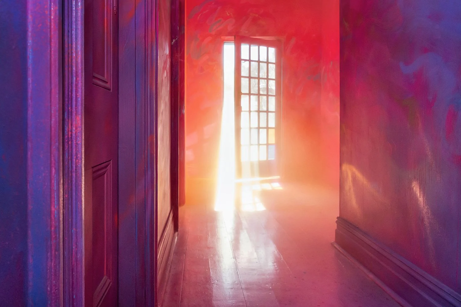 Light shines through a glass front door, causing yellow smoke to appear glowing. The smoke contrasts with the red painted immersive mural.