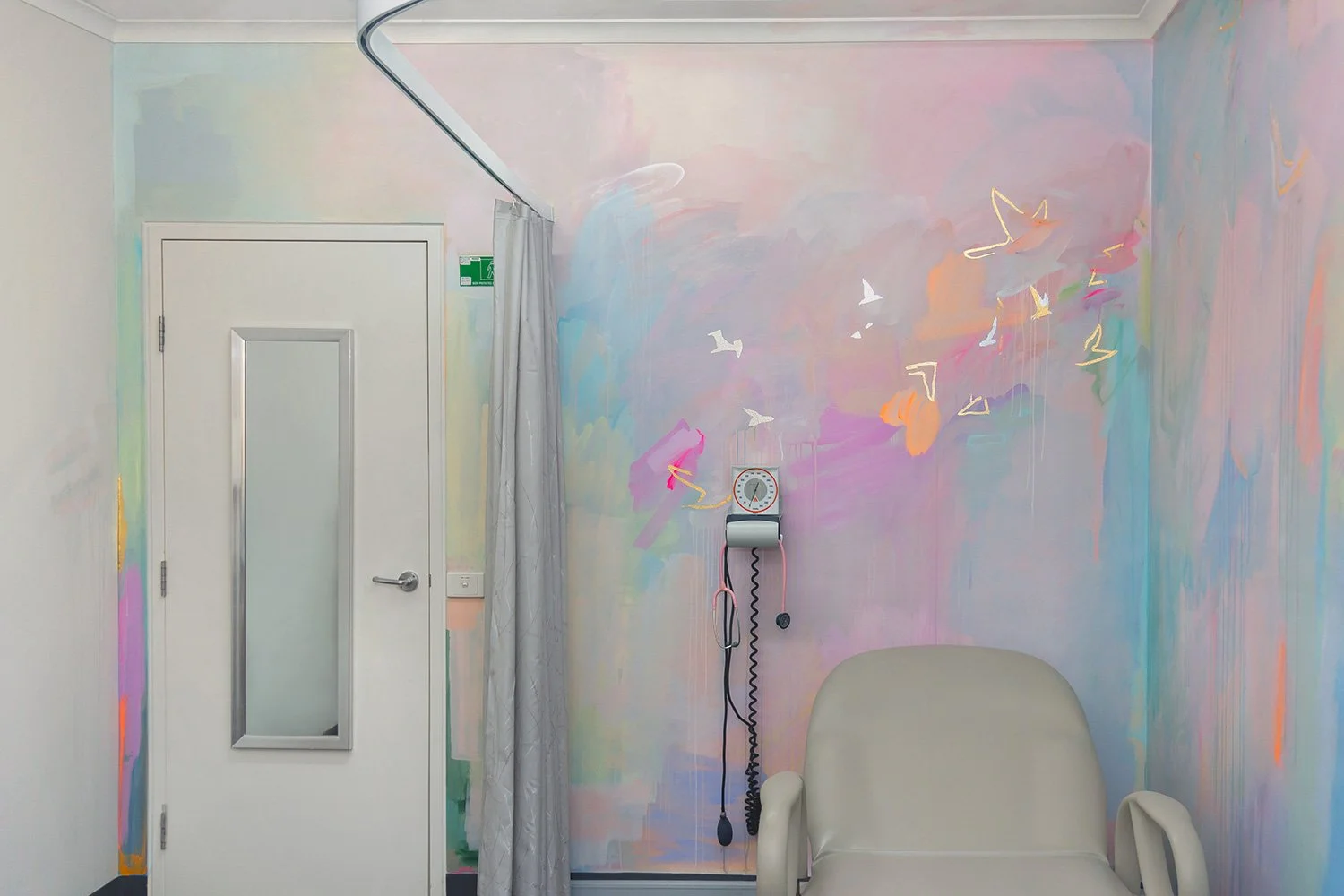 Pastel abstract mural painted in an OB/GYN office, featuring pink stethoscope and medical equipment. Gold and silver gilded birds and geometric shapes fly across the wall.