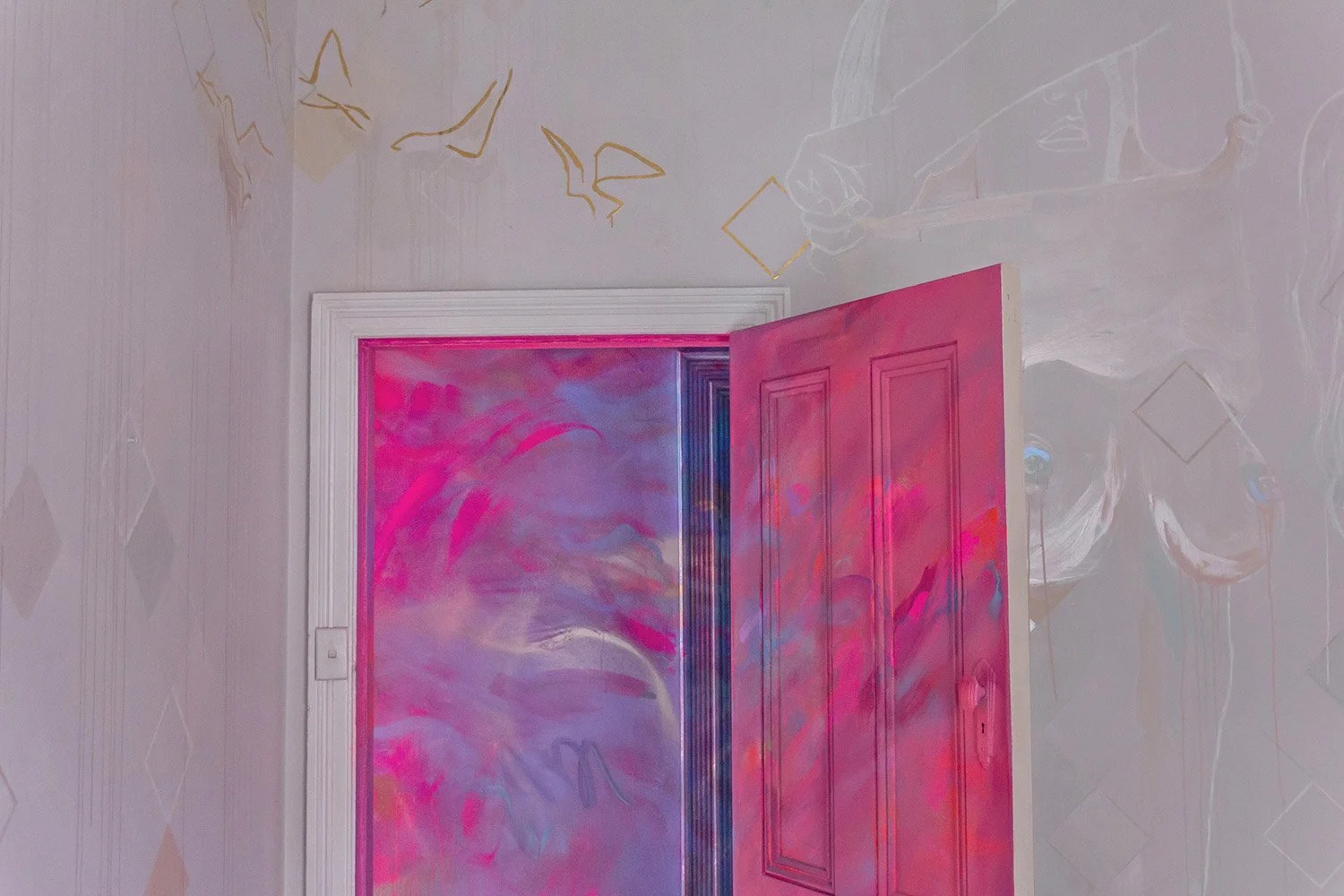 A nude painted female figure is painted on a bedroom wall, next to her a door opens to reveal a bright purple and pink painted hallway.