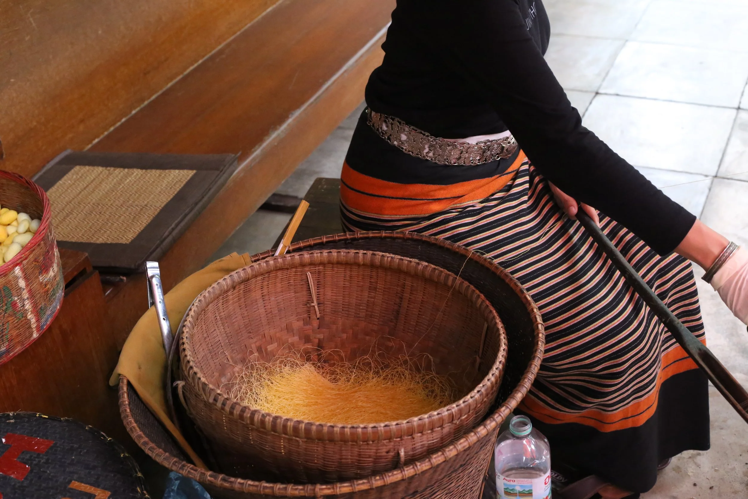 this woman was taking a basket of silk and using the spool to her right to spin it into scarves, shirts and other things for the jim thompson store and foundation.