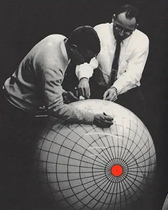 Two men looking at a large spherical object with a grid pattern and a red dot in the center, possibly a globe or scientific model.