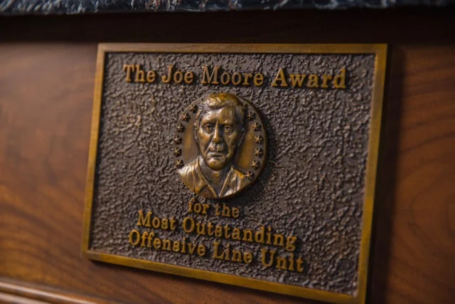 The trophy’s bas-relief includes the likeness of Joe Moore, considered one of the greatest offensive line coaches in college football history