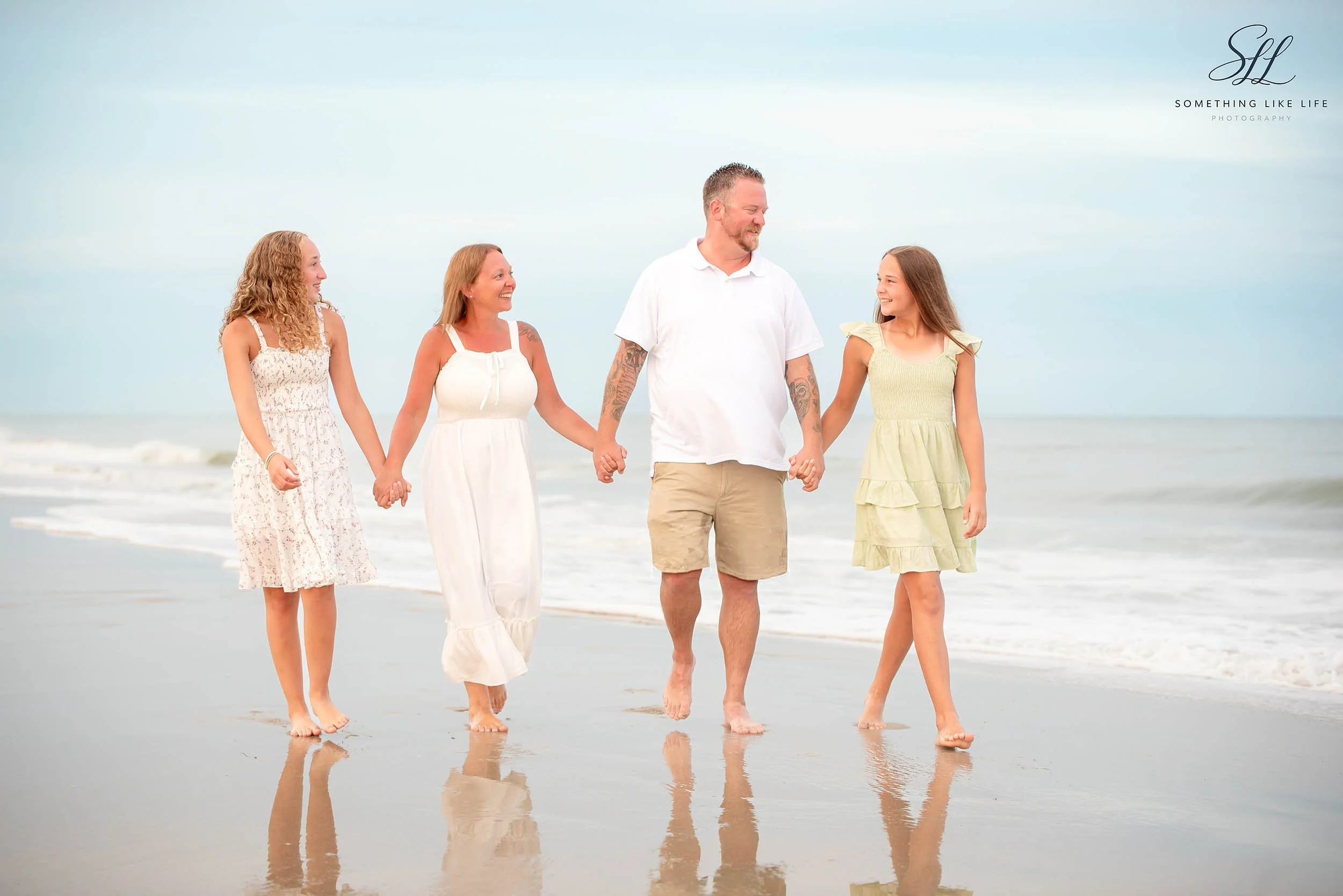 A family walking hand in hand along the shoreline during their Myrtle Beach vacation, captured in soft natural light with reflections on the wet sand.