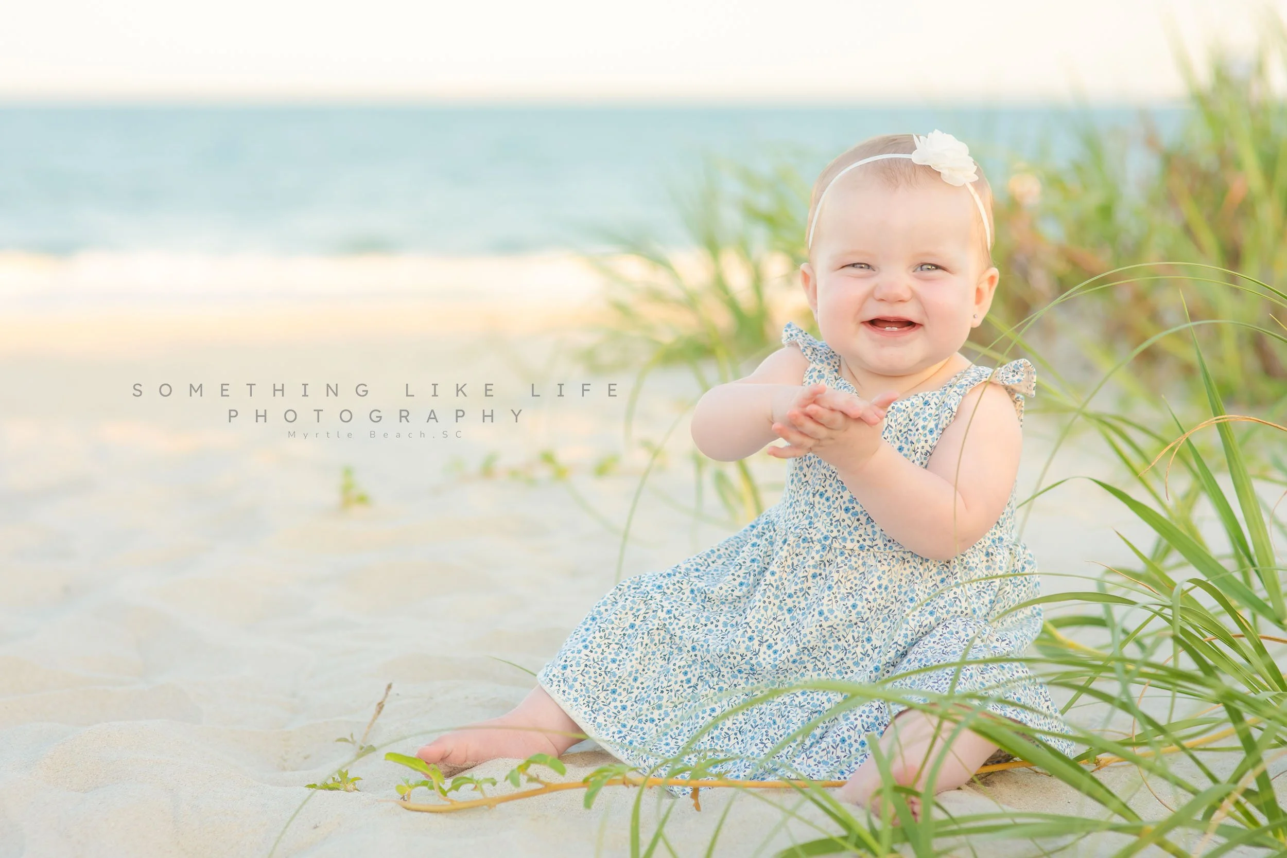  Smiling baby sitting in sand at sunset during Myrtle Beach family photoshoot. 