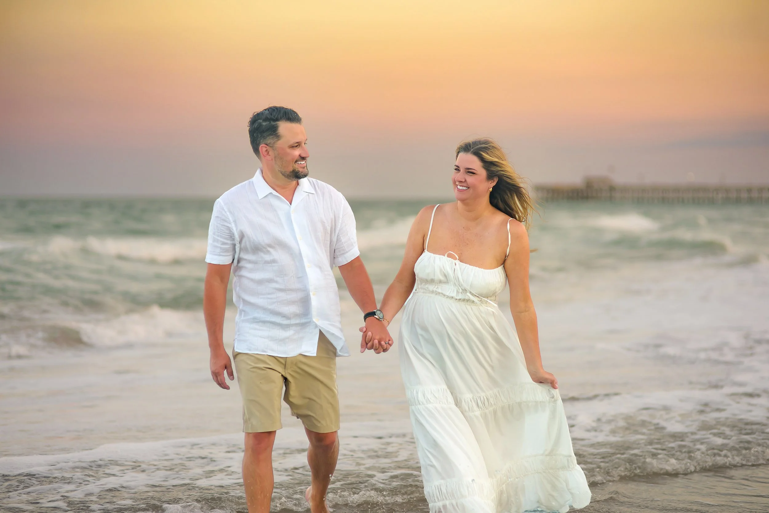 Mom and Dad walk hand in hand along the shore at sunset.