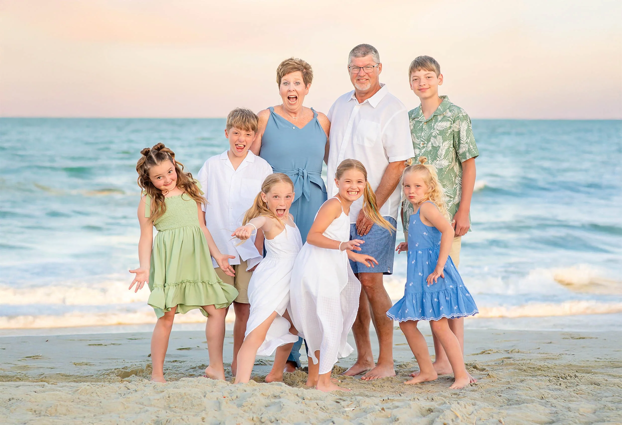 Extended family laughing and posing playfully during a Myrtle Beach family photo session, wearing coordinated coastal outfits while enjoying a fun, relaxed moment by the ocean at sunset.