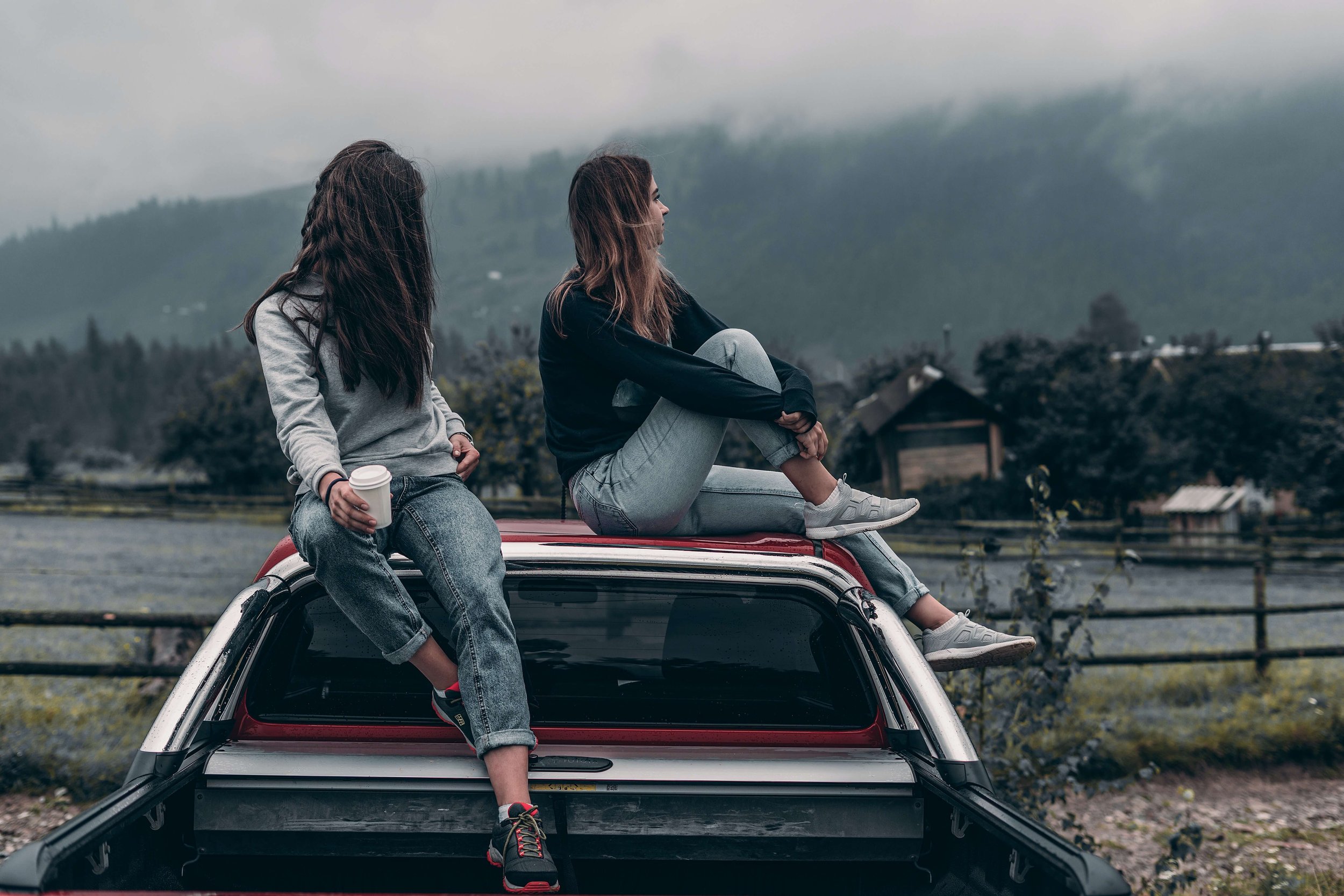 Two young women sit on top of a car as they ponder the future. Therapy for Young Adults in NYC can help guide you through these transformative years.