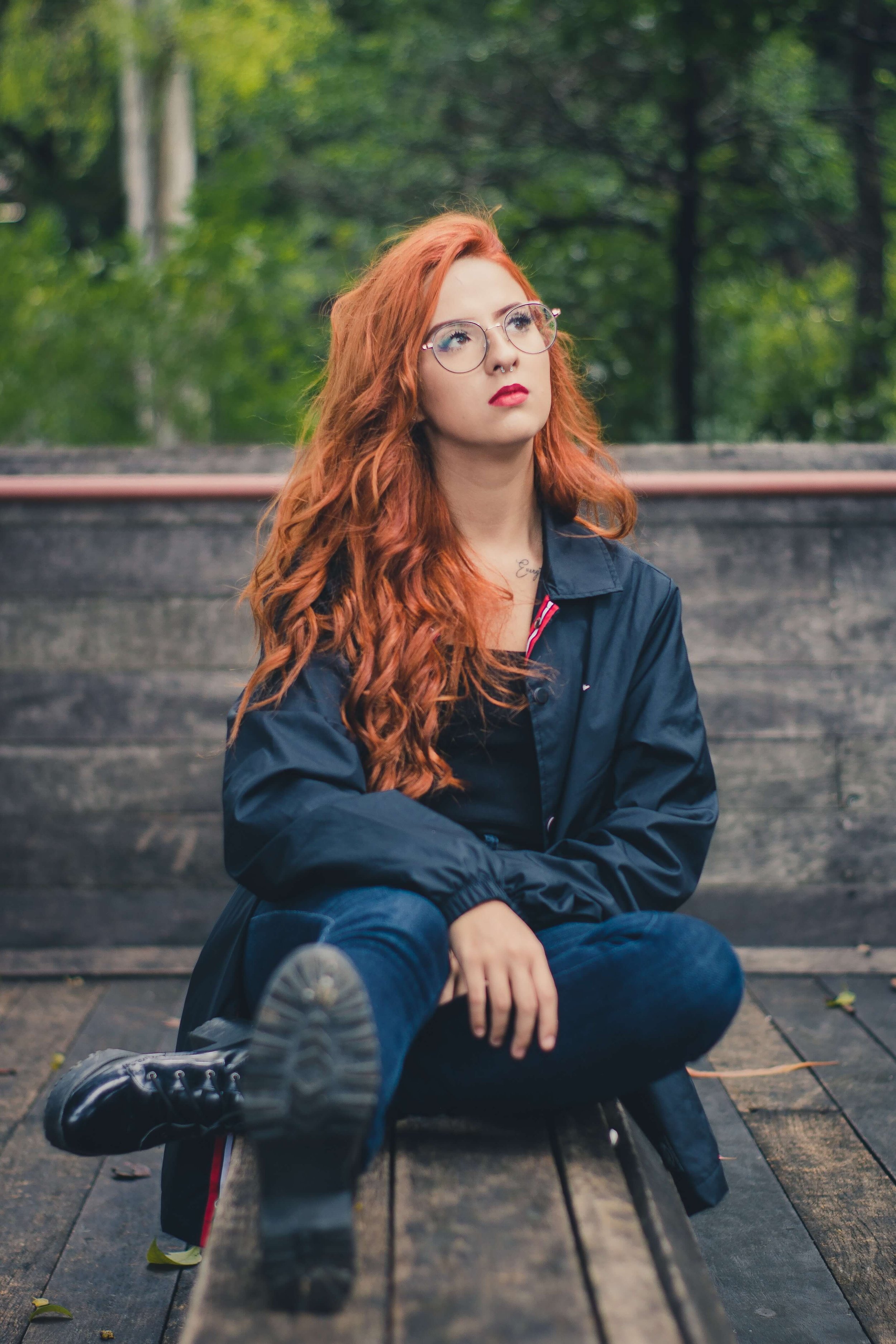 A red headed young woman sits on bench looking toward the sky representing someone struggling with Seasonal Affective Disorder as the seasons change from summer to fall. Reach out to a Young Adult Therapist in NYC for help.