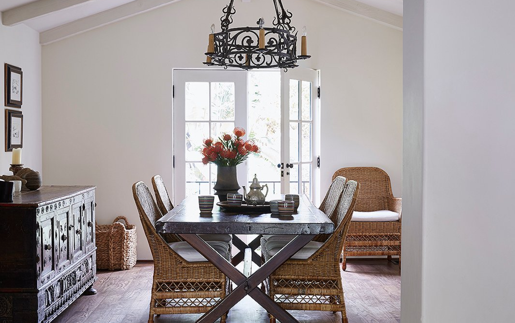 “This is the family table,” says Kendall. “We have dinner, the girls do their homework.” It was reimagined from an antique Spanish door. The rattan chairs add airy space. A vase by potter Miri Mara sits near striped cups by a local artisan.