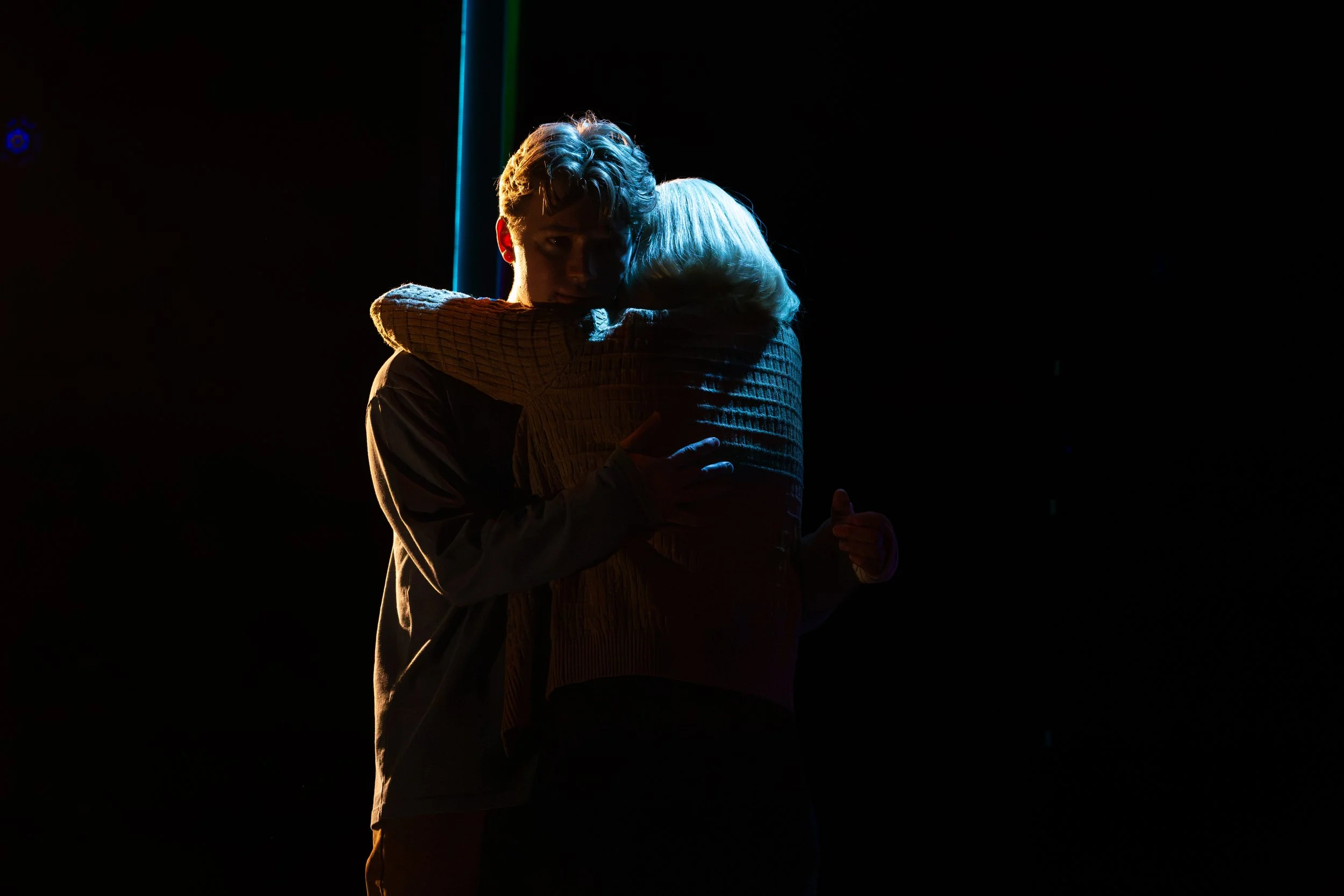 Two people hugging in dim lighting, with one person's face partially visible and illuminated, creating a silhouette effect. Maggie Bera playing Cynthia Murphy in Dear Evan Hansen at the Engeman Theatre.
