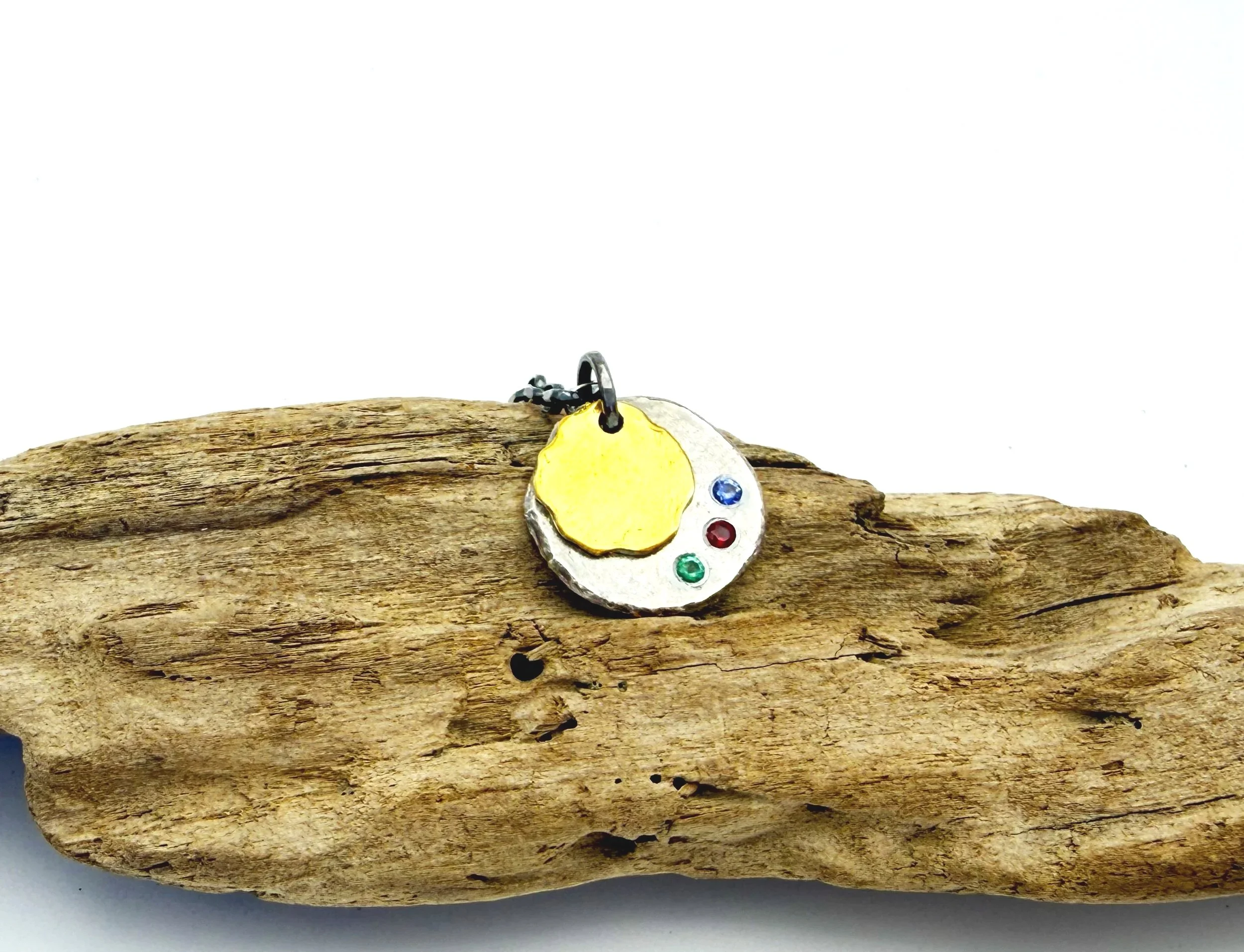 Birthstone disc pendant resting on driftwood