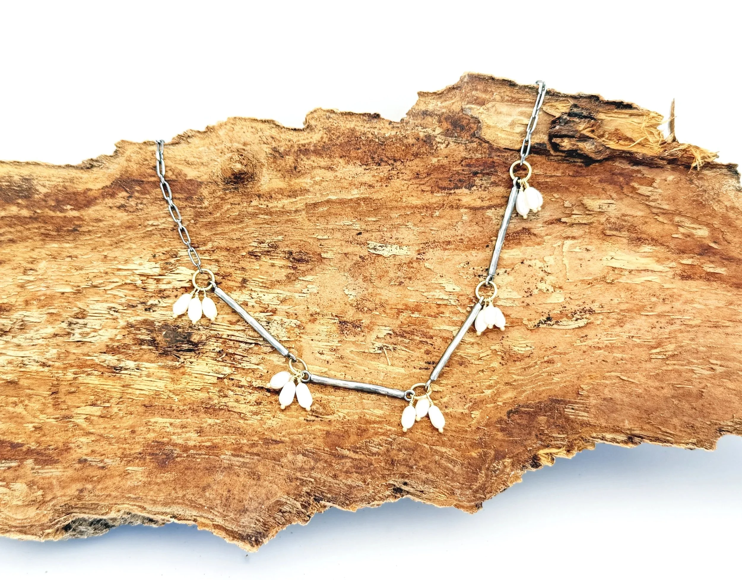 Pearl drops and oxidized silver bars on textured bark