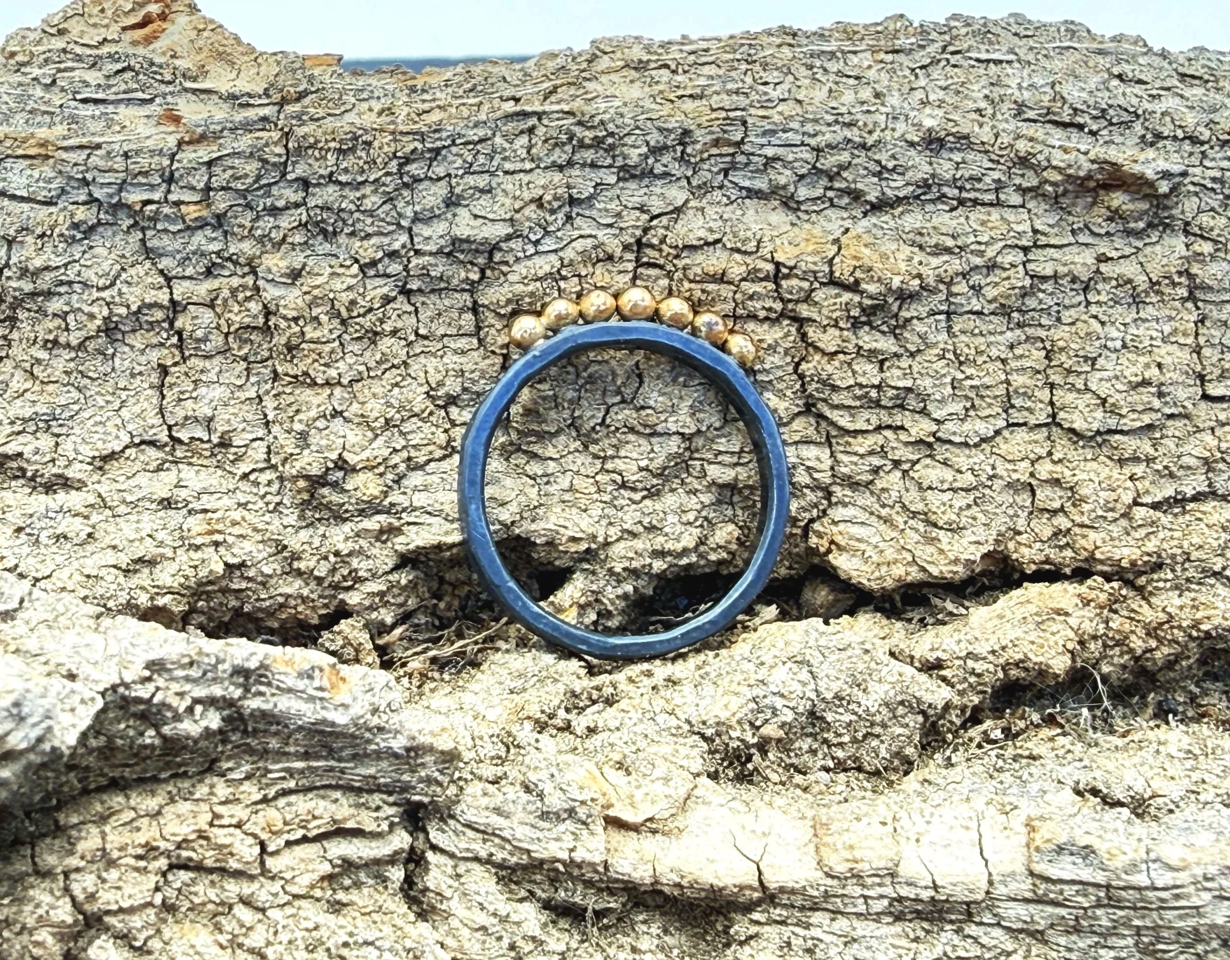 Oxidized hammered silver ring leaning on weathered stone, gold dots along the top