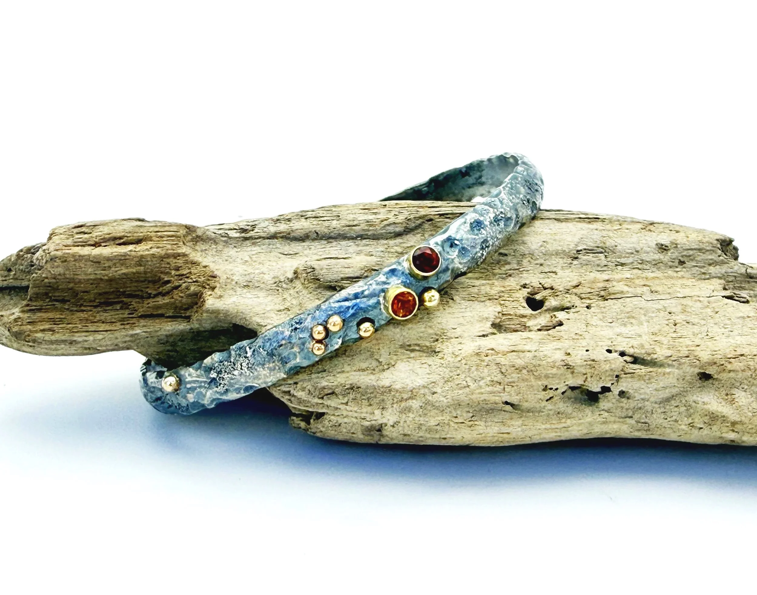 Hammered silver cuff with garnet and citrine resting on driftwood