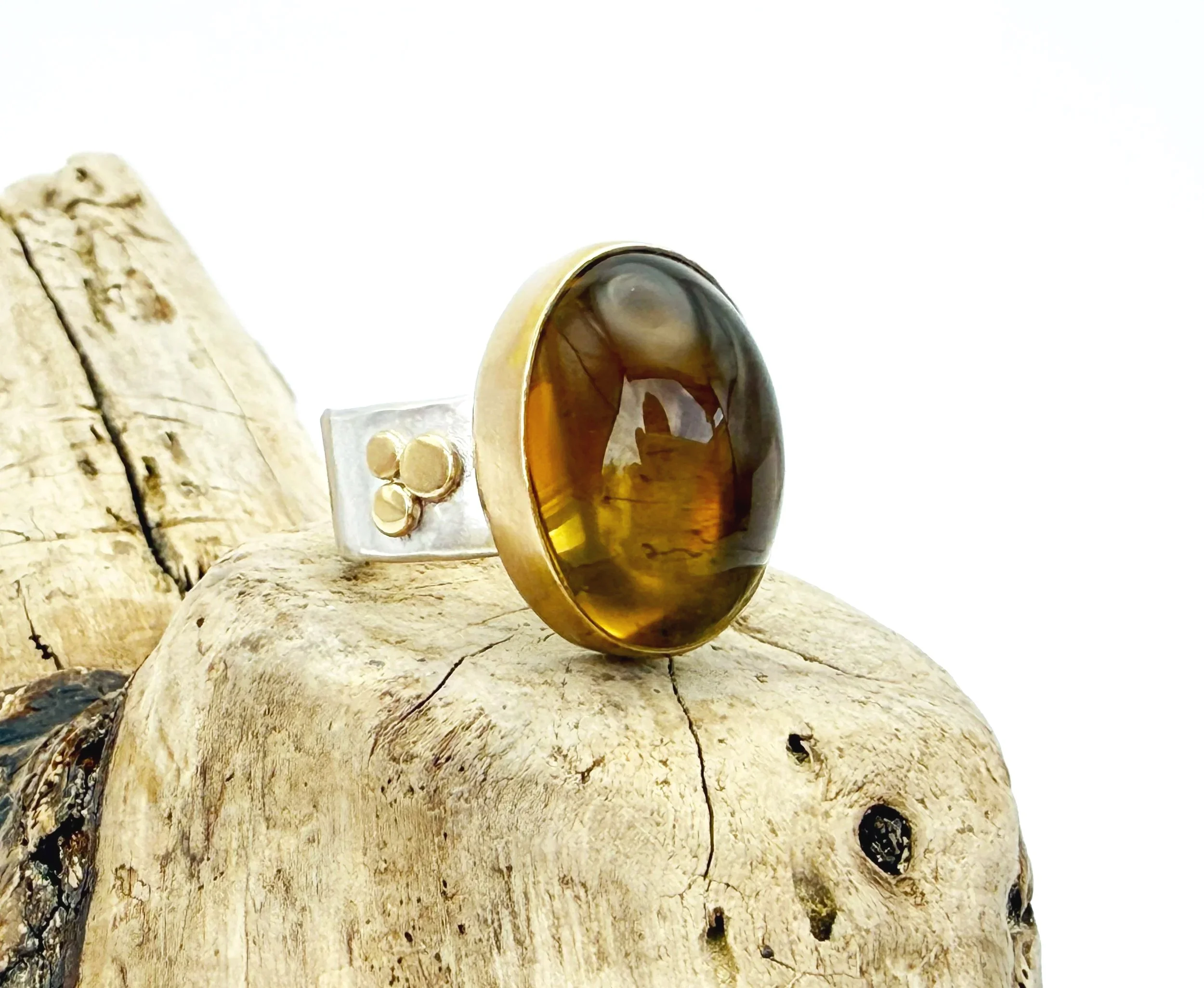 Citrine ring with gold bezel and silver band resting on driftwood
