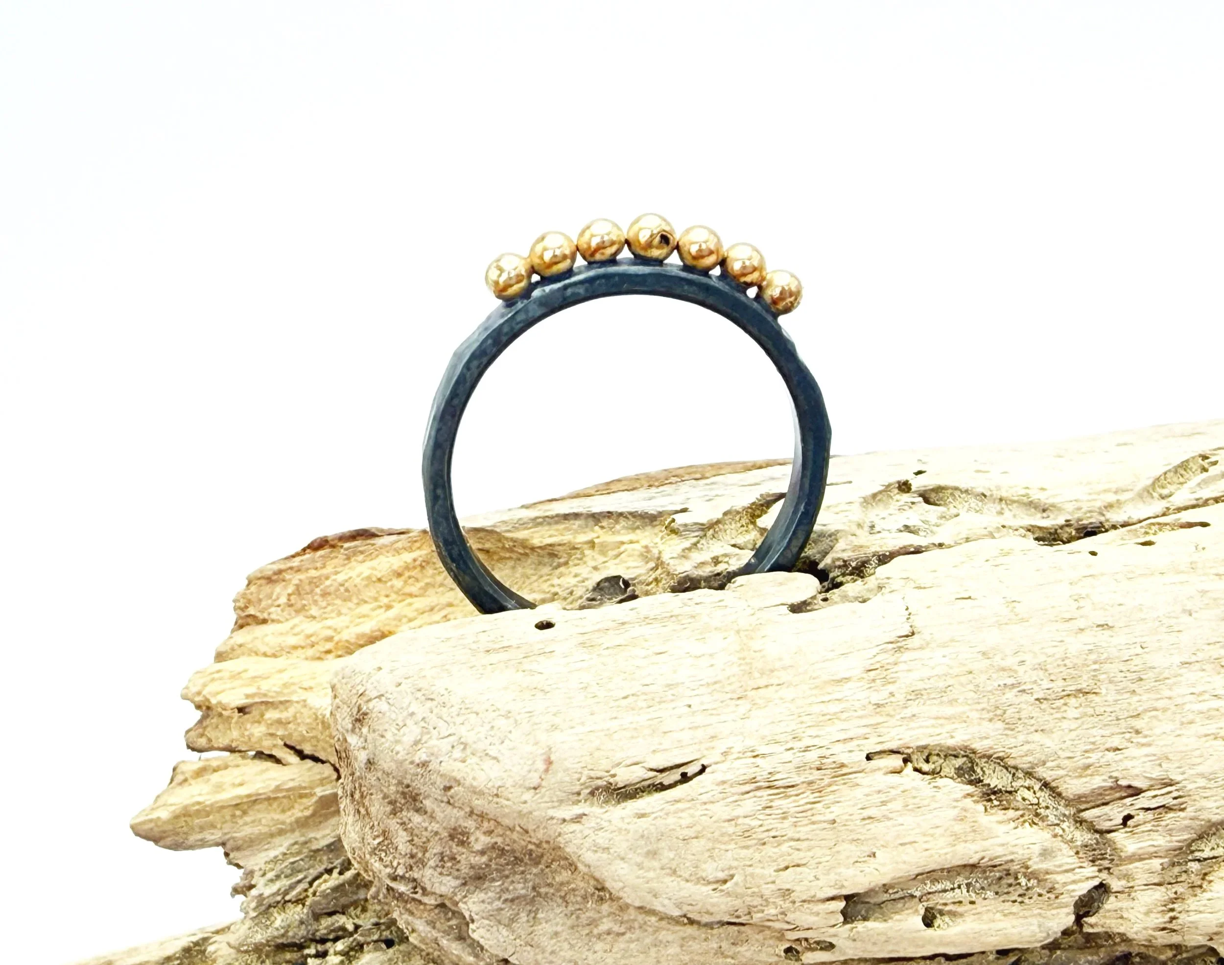 Oxidized silver ring with 14k gold dots resting on driftwood