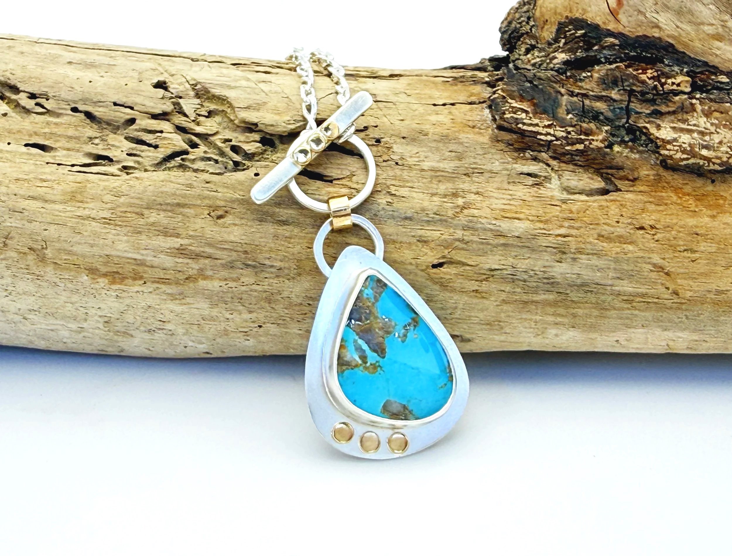 Blue Gem turquoise teardrop pendant with a sterling silver and 14k gold toggle, on driftwood