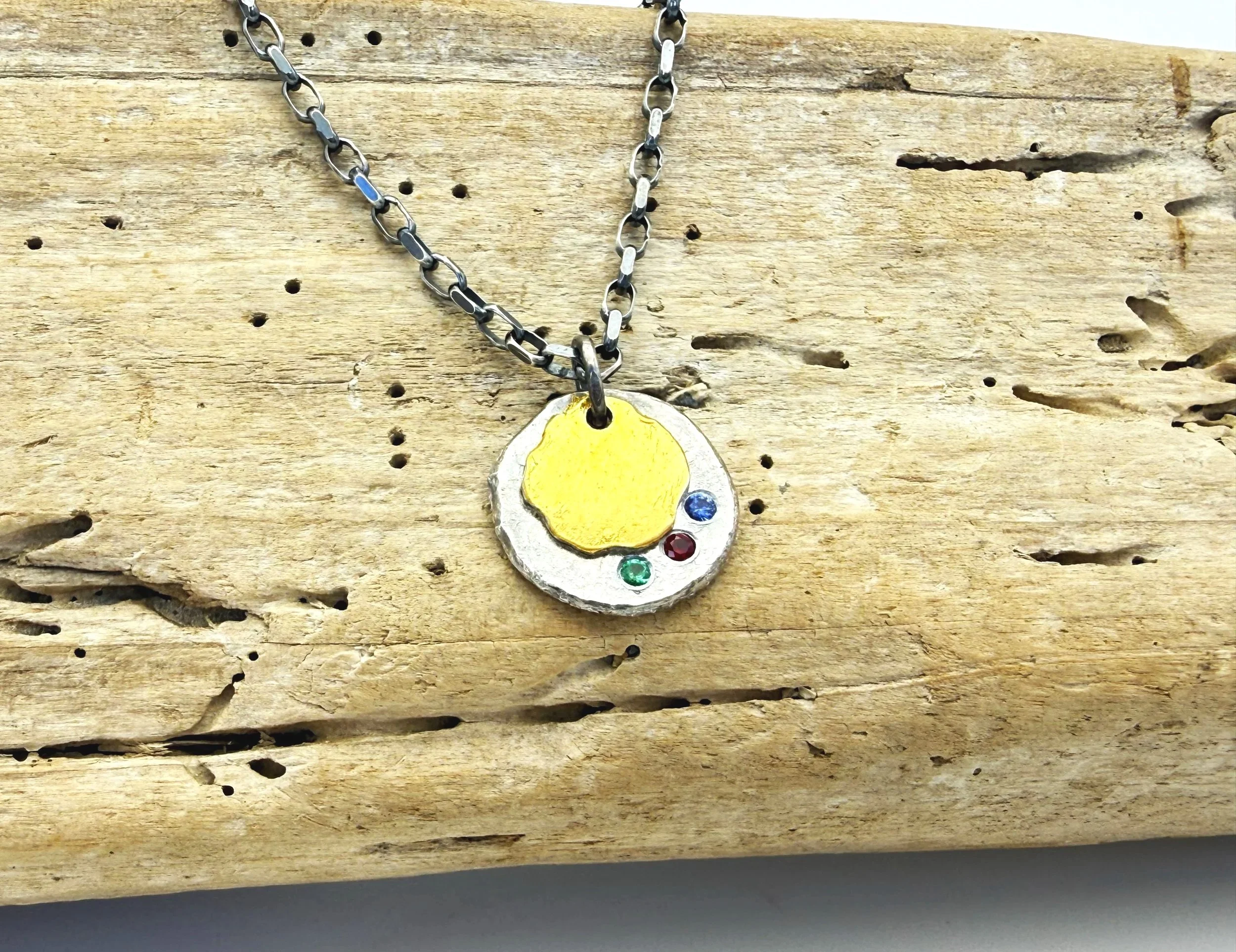 Hammered silver disc pendant with sapphire, ruby and emerald on driftwood