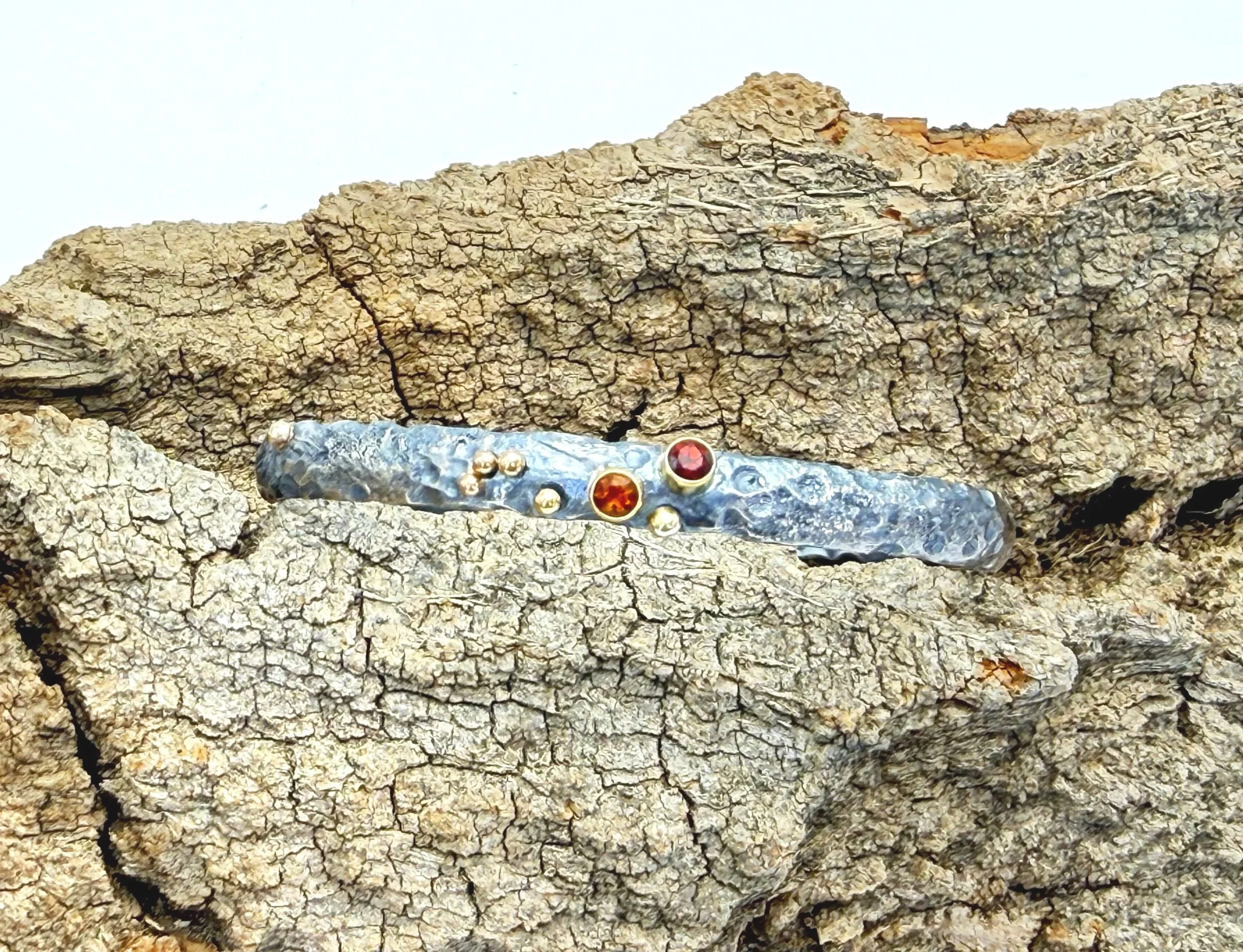 Silver cuff with garnet and citrine set in 14k gold, on weathered stone