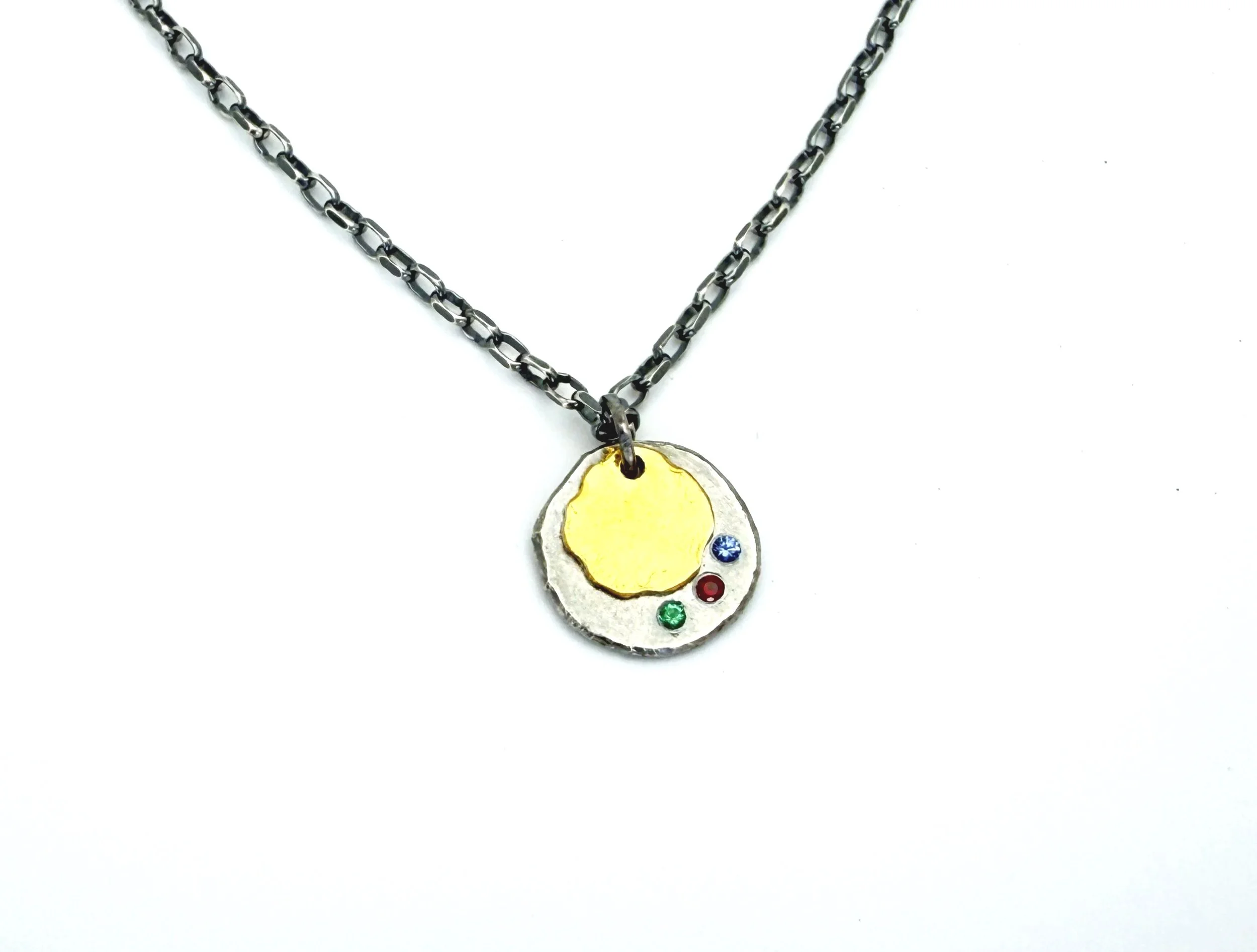 Close-up of the silver disc pendant with 24k gold leaf and three 2mm gemstones, on white